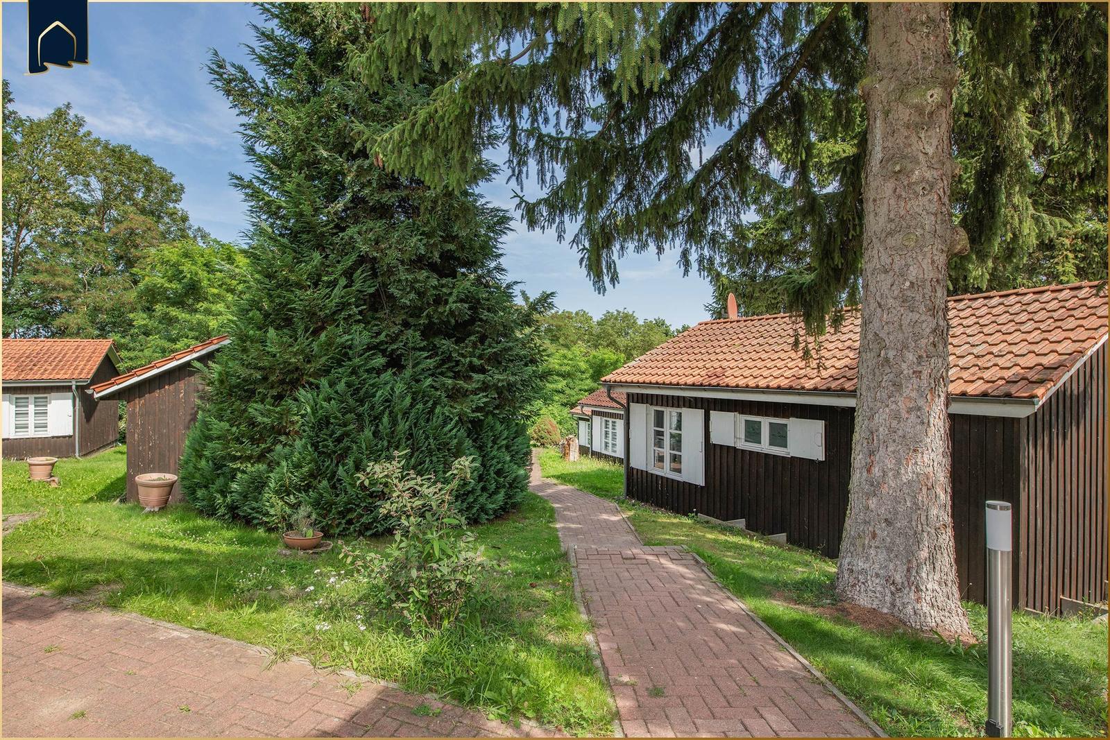 Wohnhaus mit Holzfassade und Ziegeldach. Gartenweg und große Nadelbäume sichtbar.