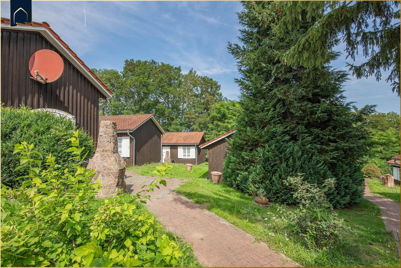 Haus mit Steinmauer, Gartenweg und Bäumen unter blauem Himmel.