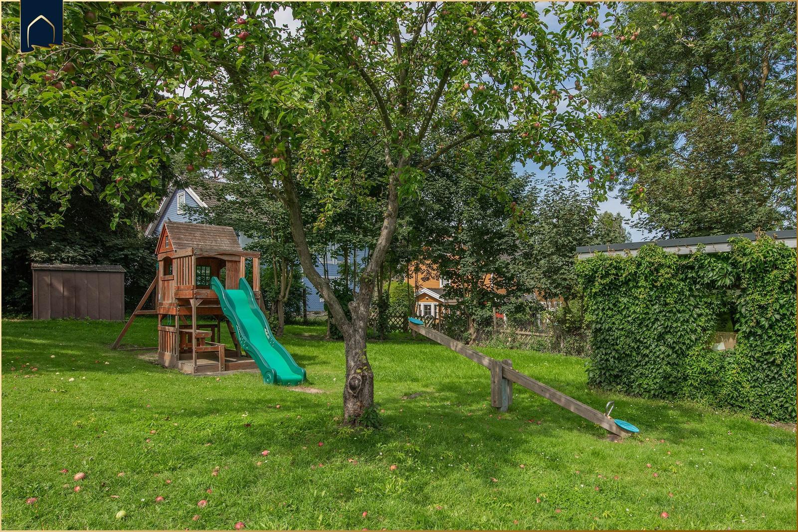 Hinterhof mit Spielplatz, Schaukel und Apfelbaum. Grasfläche und Bepflanzung sichtbar.