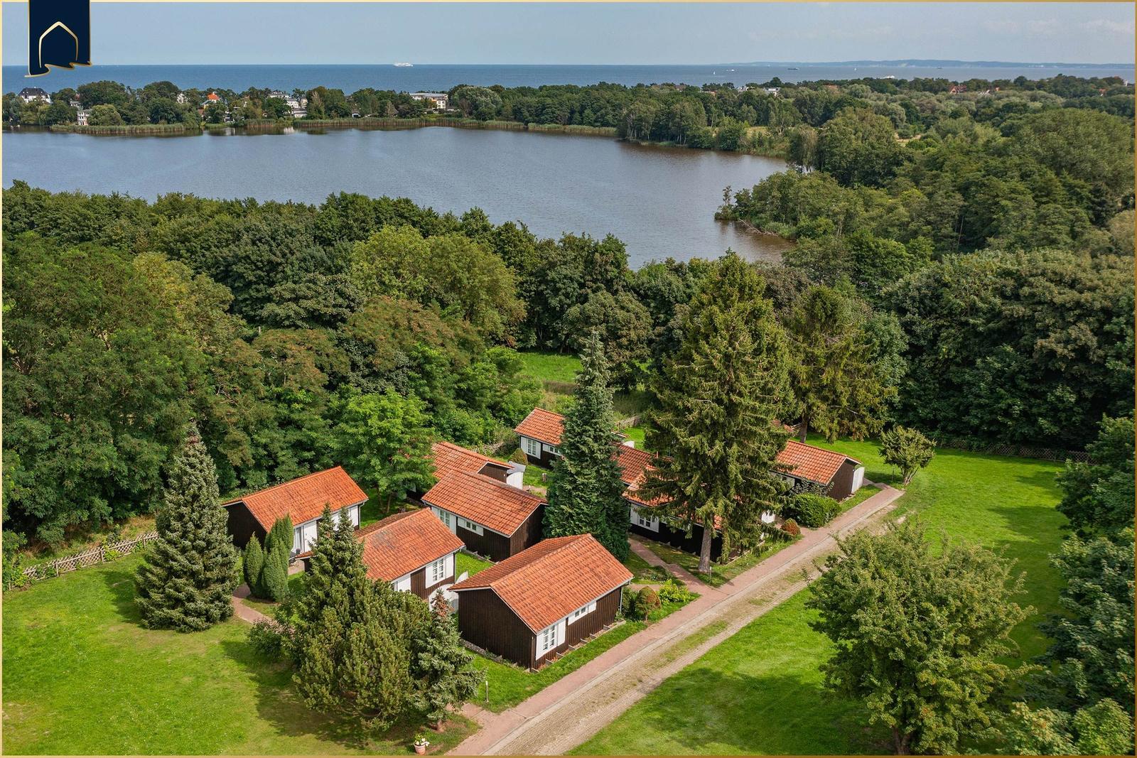 Häuser mit roten Dächern liegen in grüner Umgebung am Wasser.