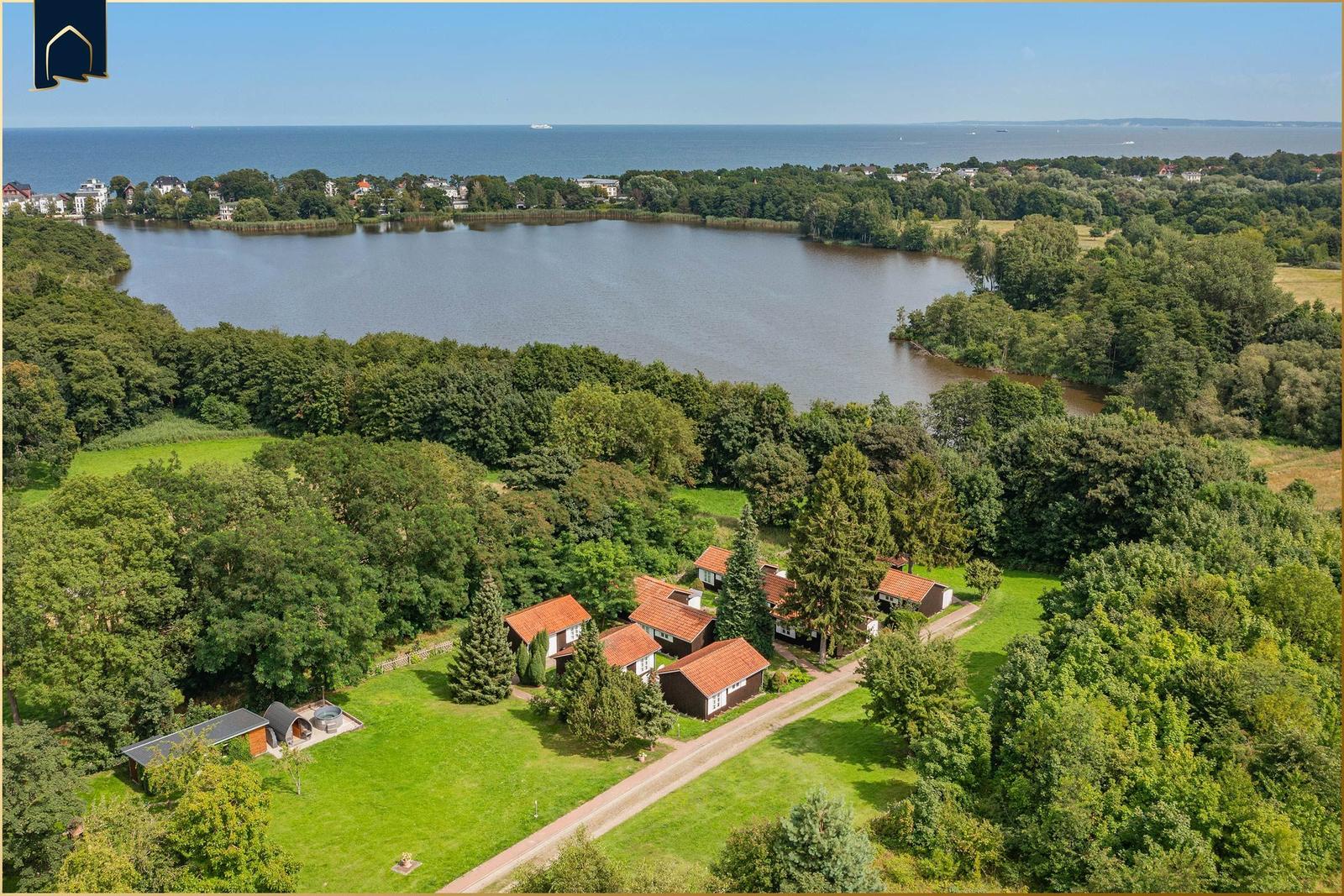 Liegenschaft mit mehreren Häusern am See, umgeben von Wald und Grünflächen.