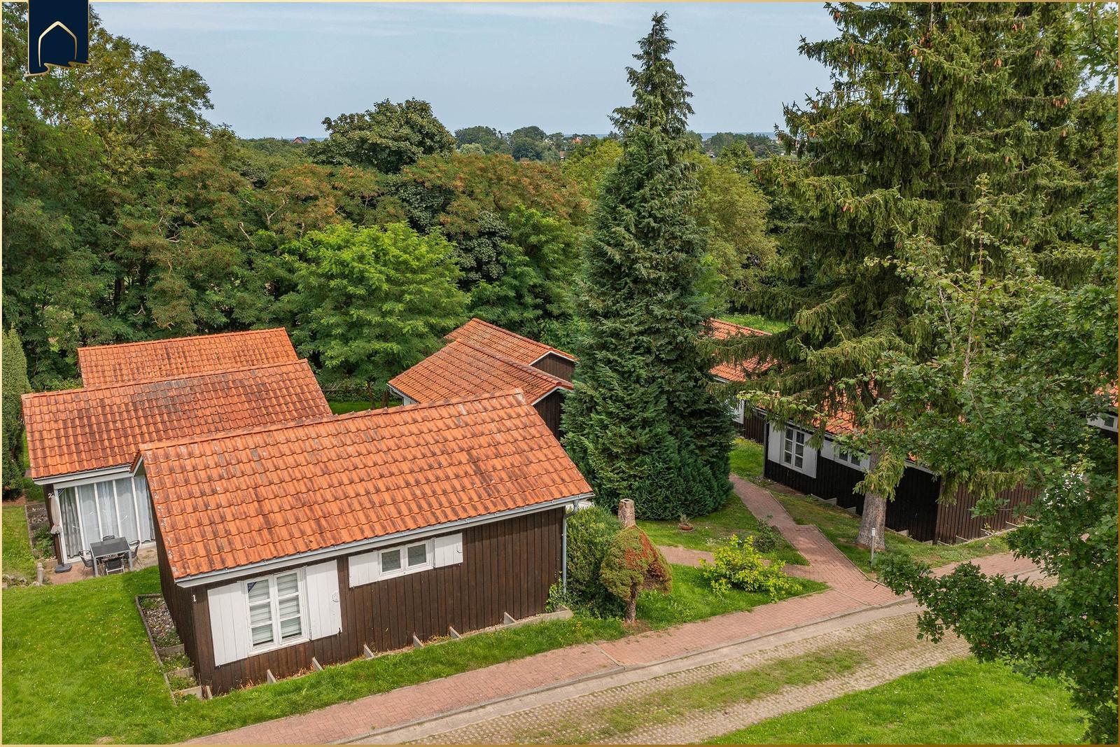 Holzhäuser mit roten Dächern in grüner Umgebung mit Wegen und Bäumen.
