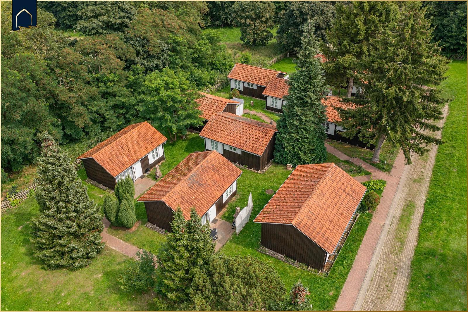 Aerial view of several wooden cabins with red tiled roofs surrounded by greenery and trees.