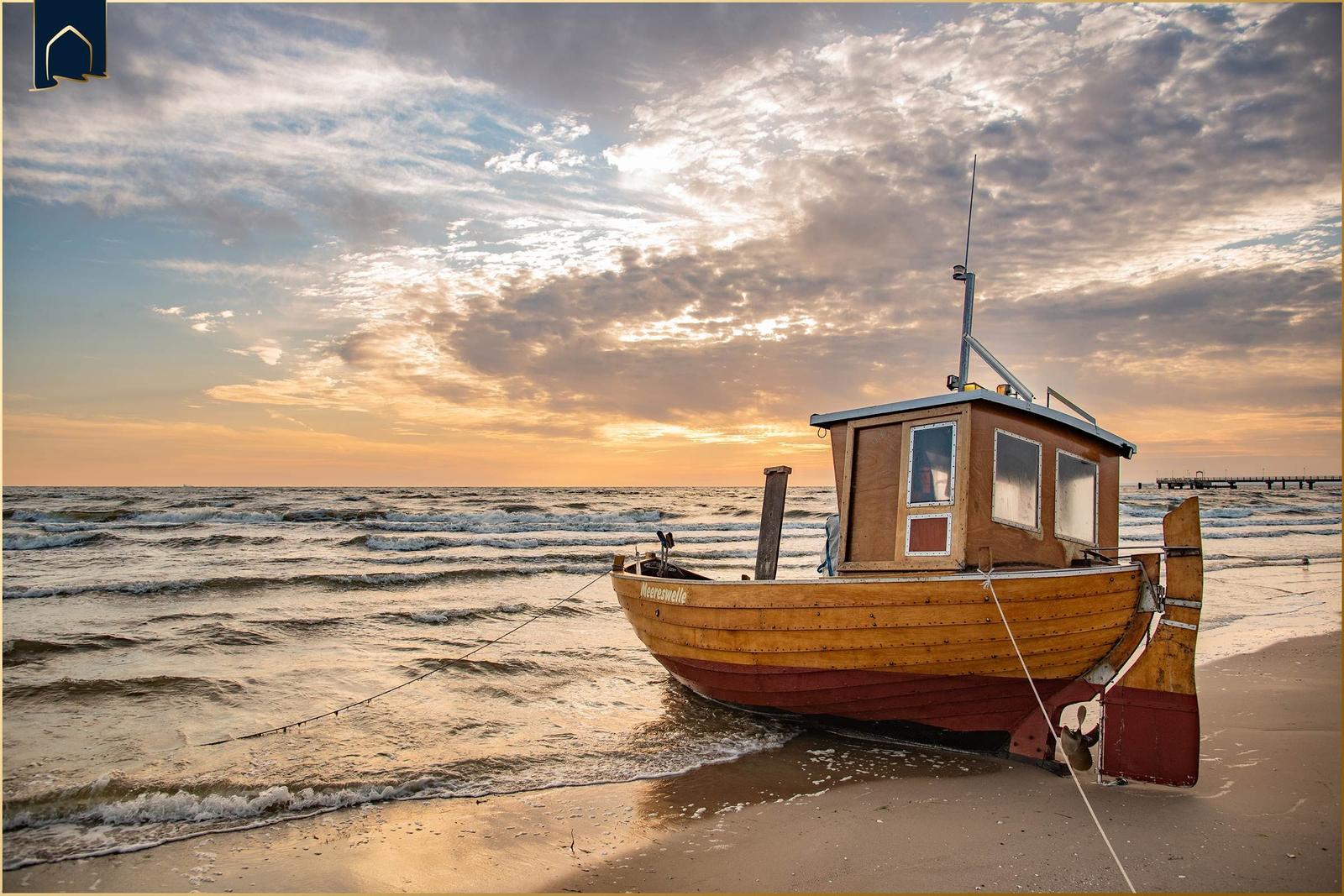 Ein hölzernes Boot mit Motorbootkabine liegt am Strand. Der Himmel ist bewölkt, das Meer wellig.