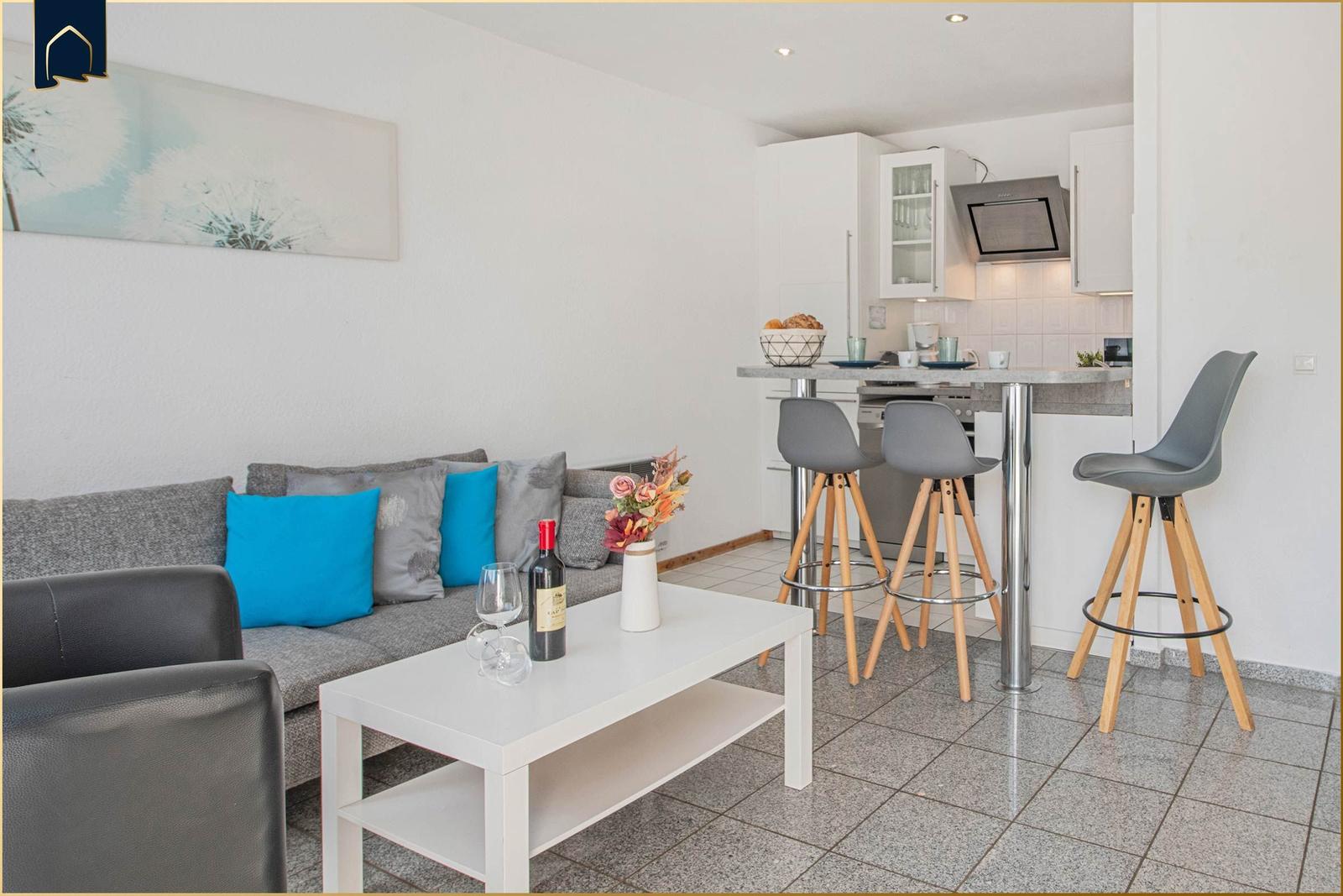 Wohnbereich mit Sofa, Couchtisch und integrierter Küchenzeile mit Barhocker.