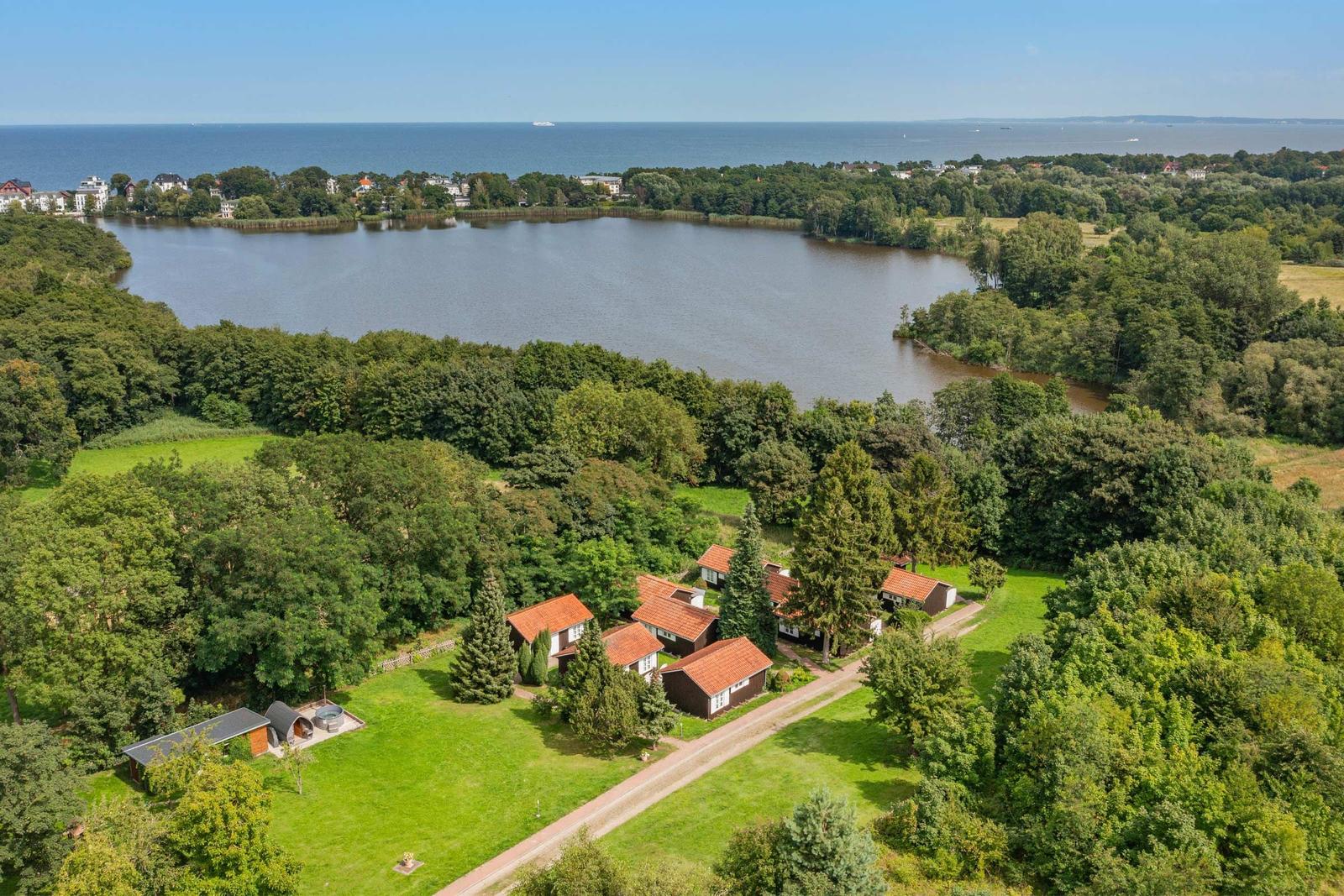 Häuser mit roten Dächern liegen am See, umgeben von Wäldern und Grünflächen.