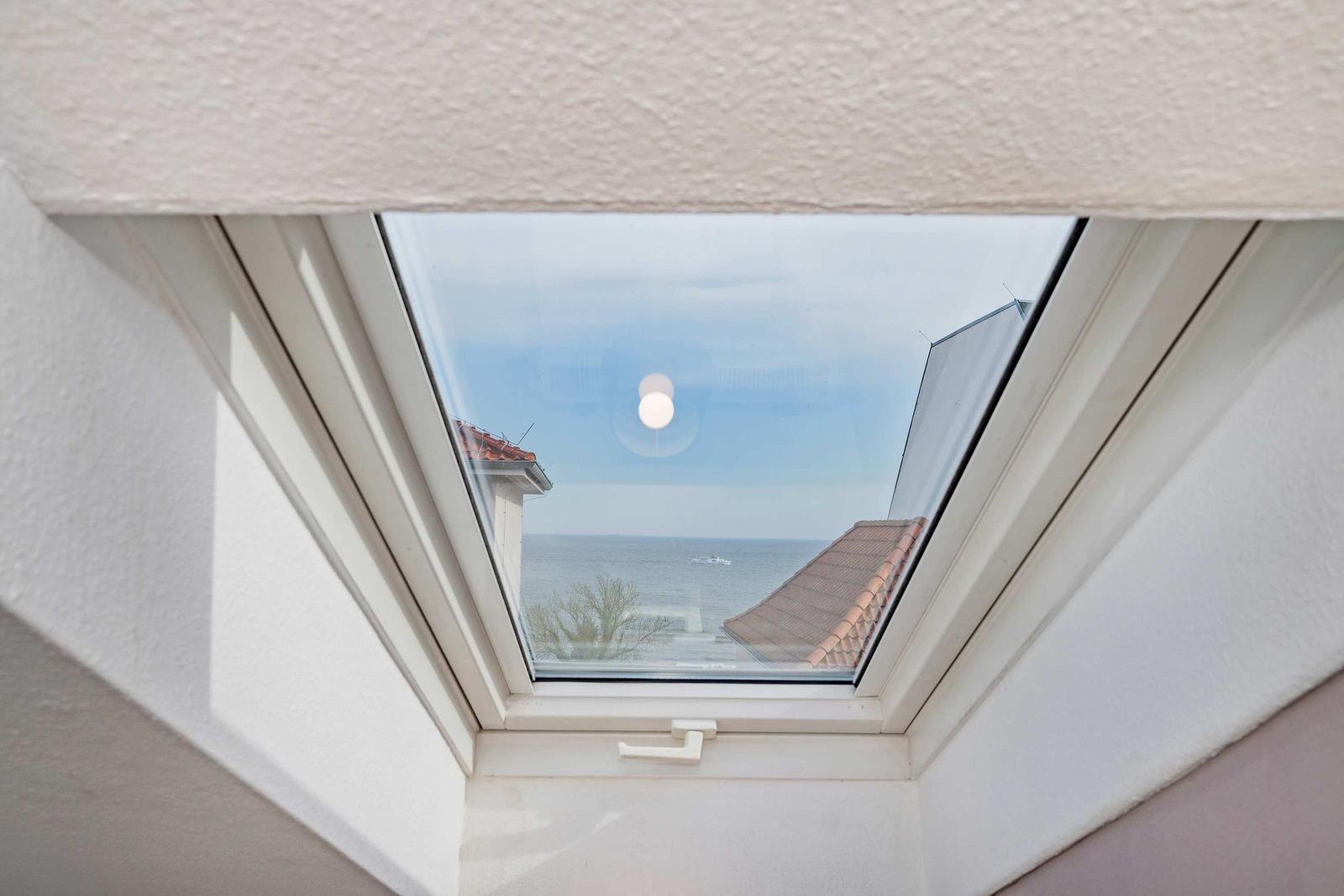 Dachfenster mit Blick auf das Meer und Dachziegel.
