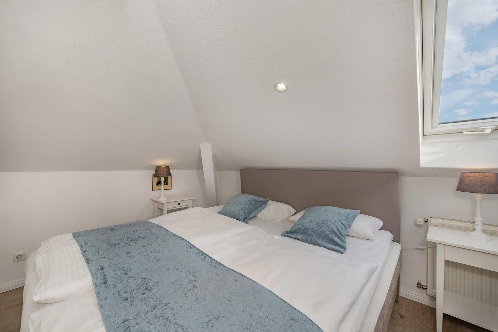 Doppelbett mit blauen Kissen und Decke, zwei Nachttische mit Lampen und Fenster.