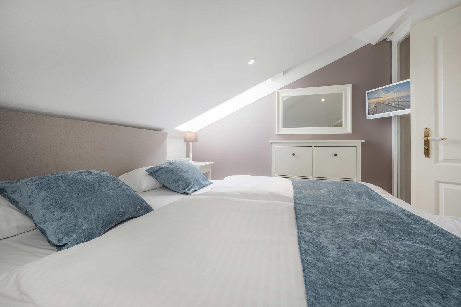 Schlafzimmer mit Dachschräge, Bett, Nachttisch, Spiegel und Kleiderschrank.
