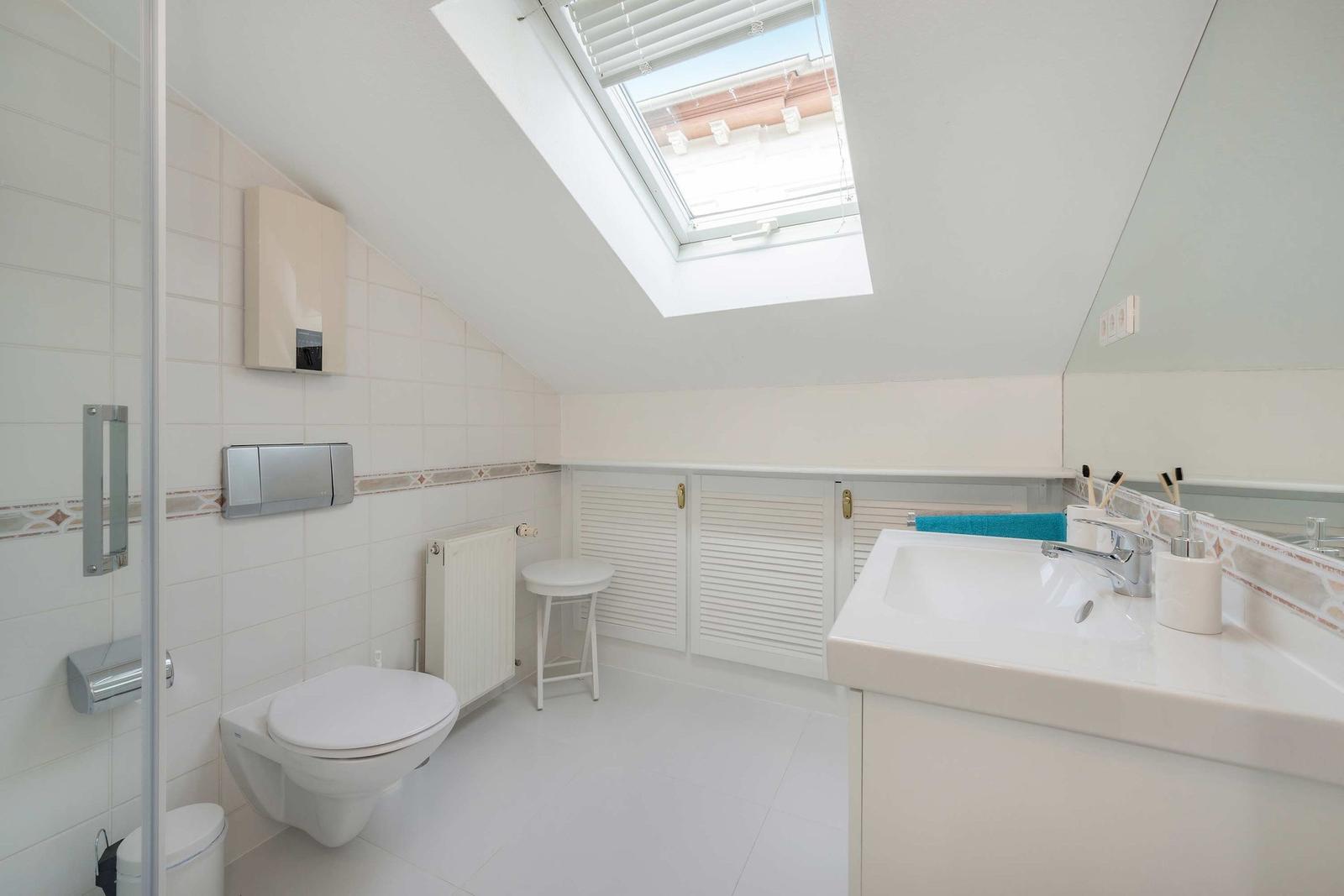Badezimmer mit Dachschrägen, Dusche, Waschbecken und Toilette unter Dach