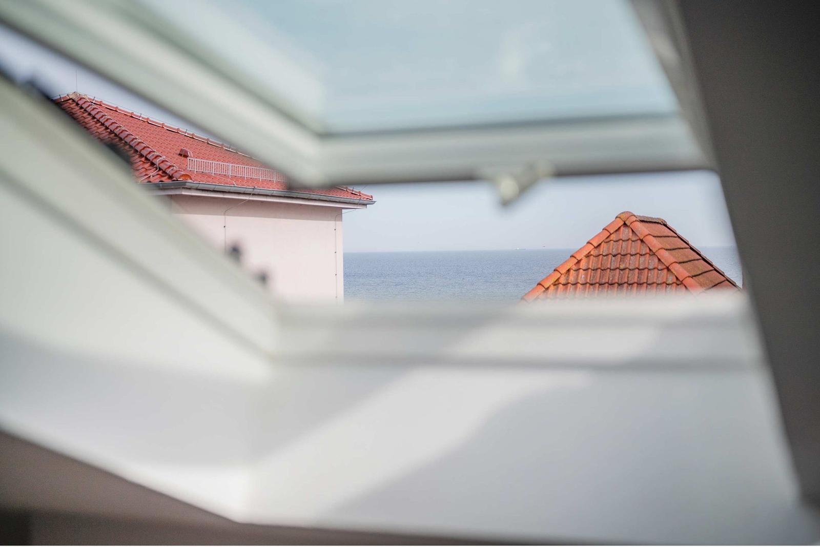 Durch das Fenster ist das Meer und zwei Dächer mit roten Ziegeln sichtbar.