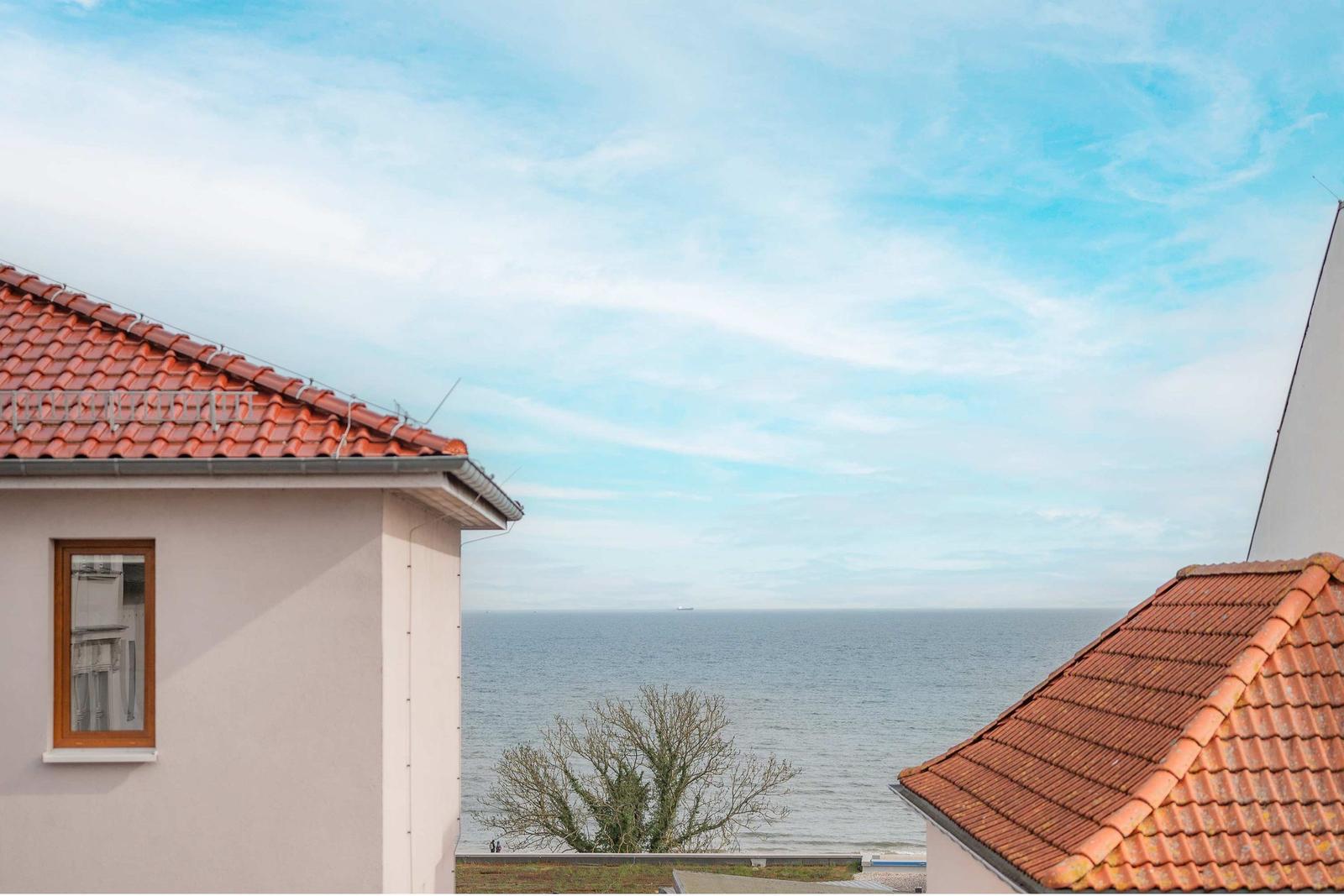 Meerblick zwischen zwei Häusern mit roten Ziegeldächern und blauem Himmel.