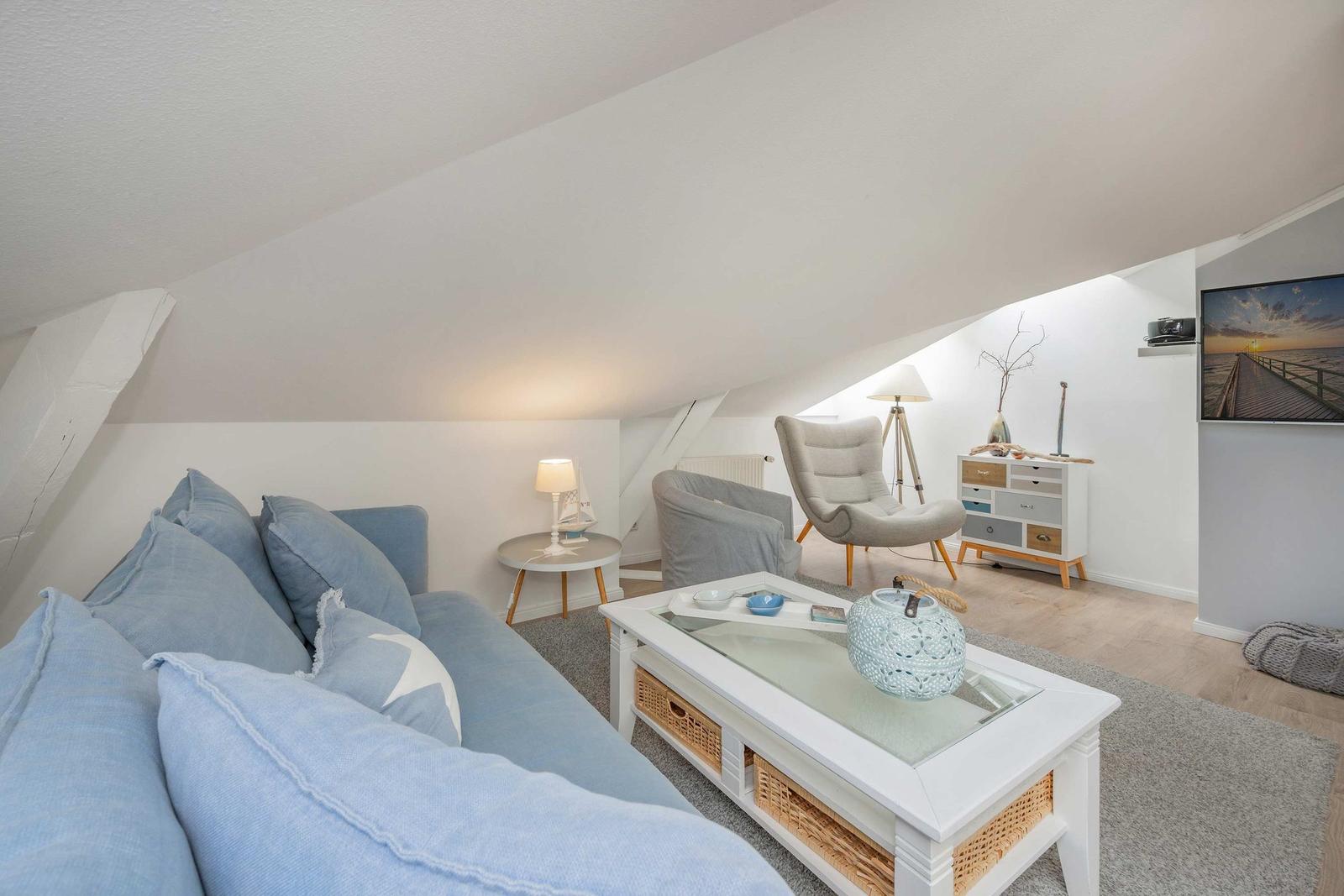 Wohnzimmer mit Sofa, Couchtisch und Sessel unter Dachschrägen.