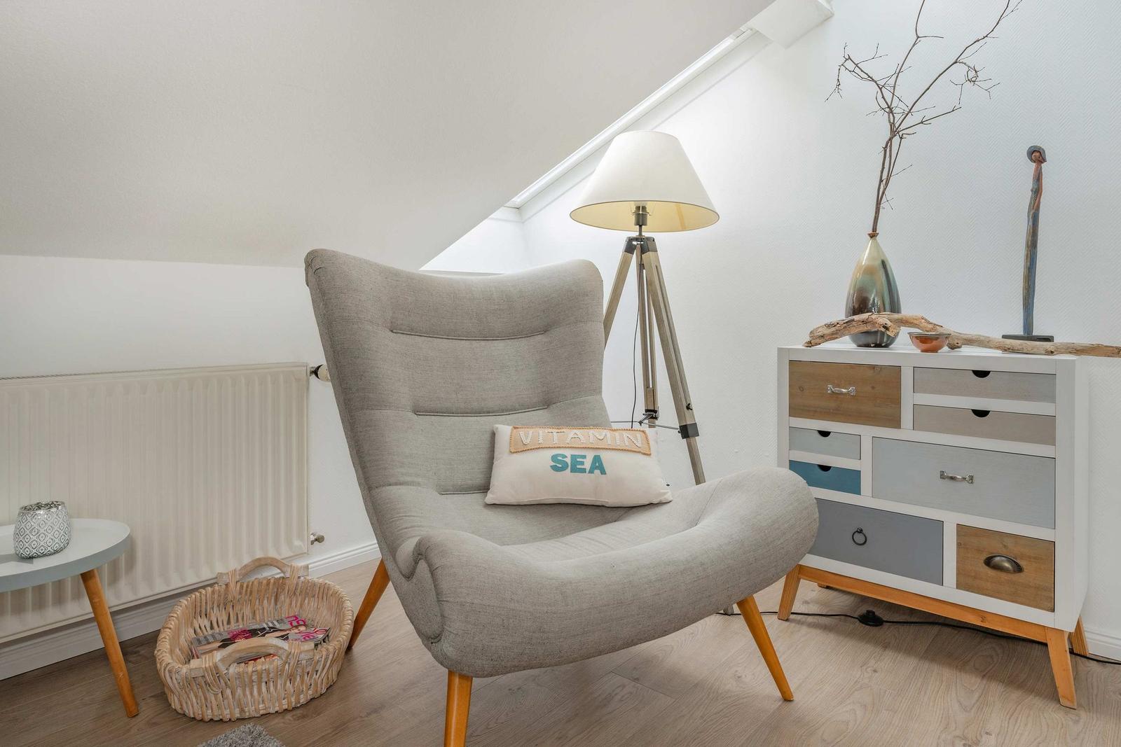 Ein grauer Sessel mit Kissen steht neben einem Schrank und einer Stehlampe.