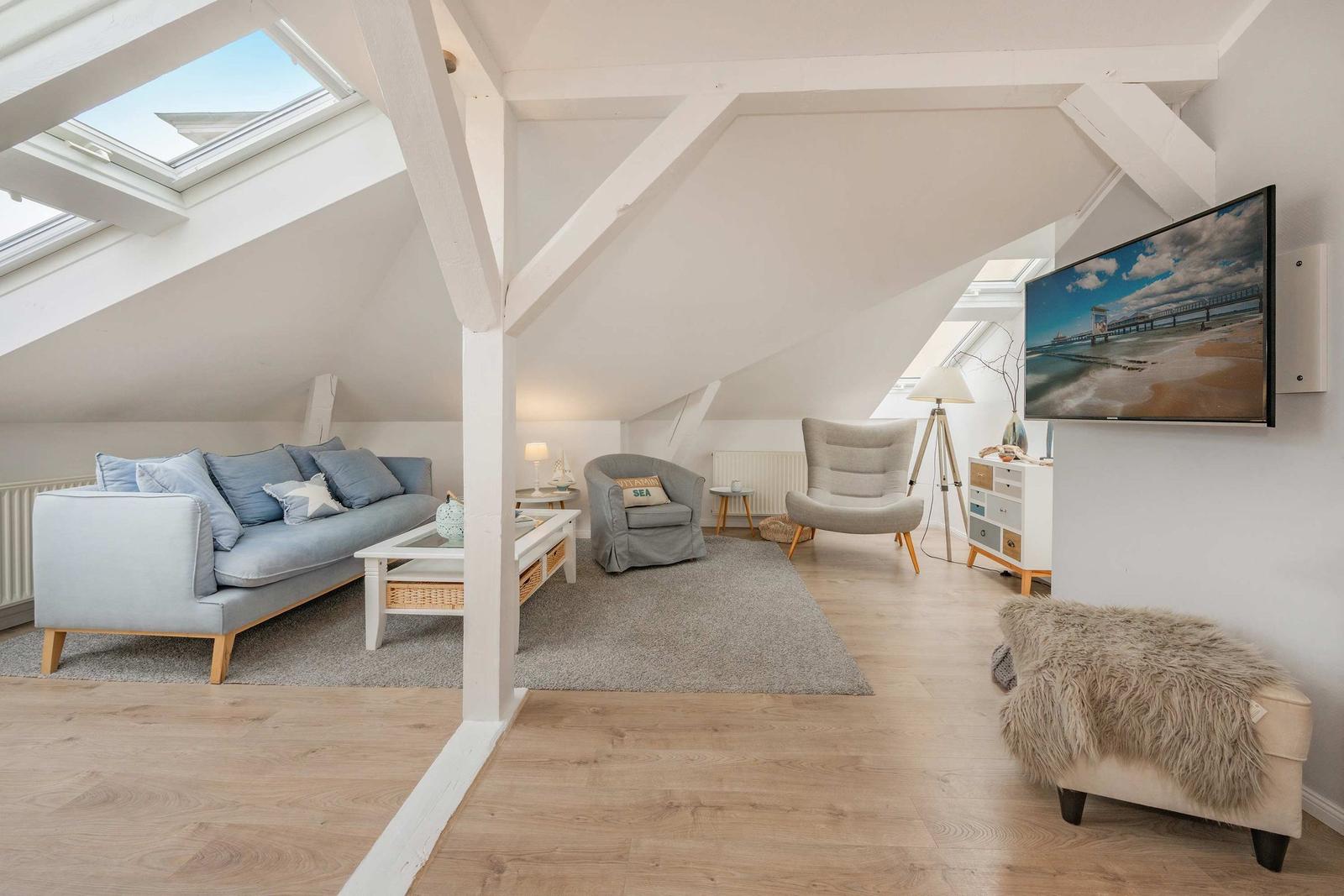 Wohnzimmer mit Sofa, Sesseln und Fernseher unter Dachschrägen mit Dachfenstern.