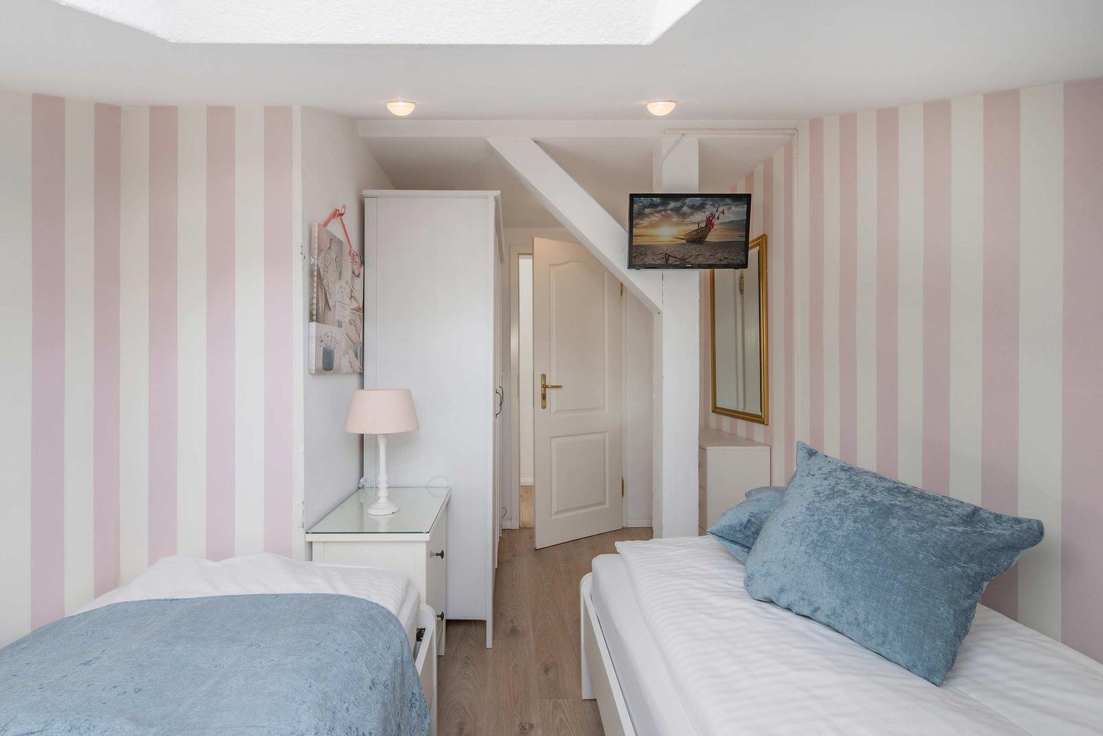 Zimmer mit zwei Betten, gestreiften Wänden und TV an der Decke.