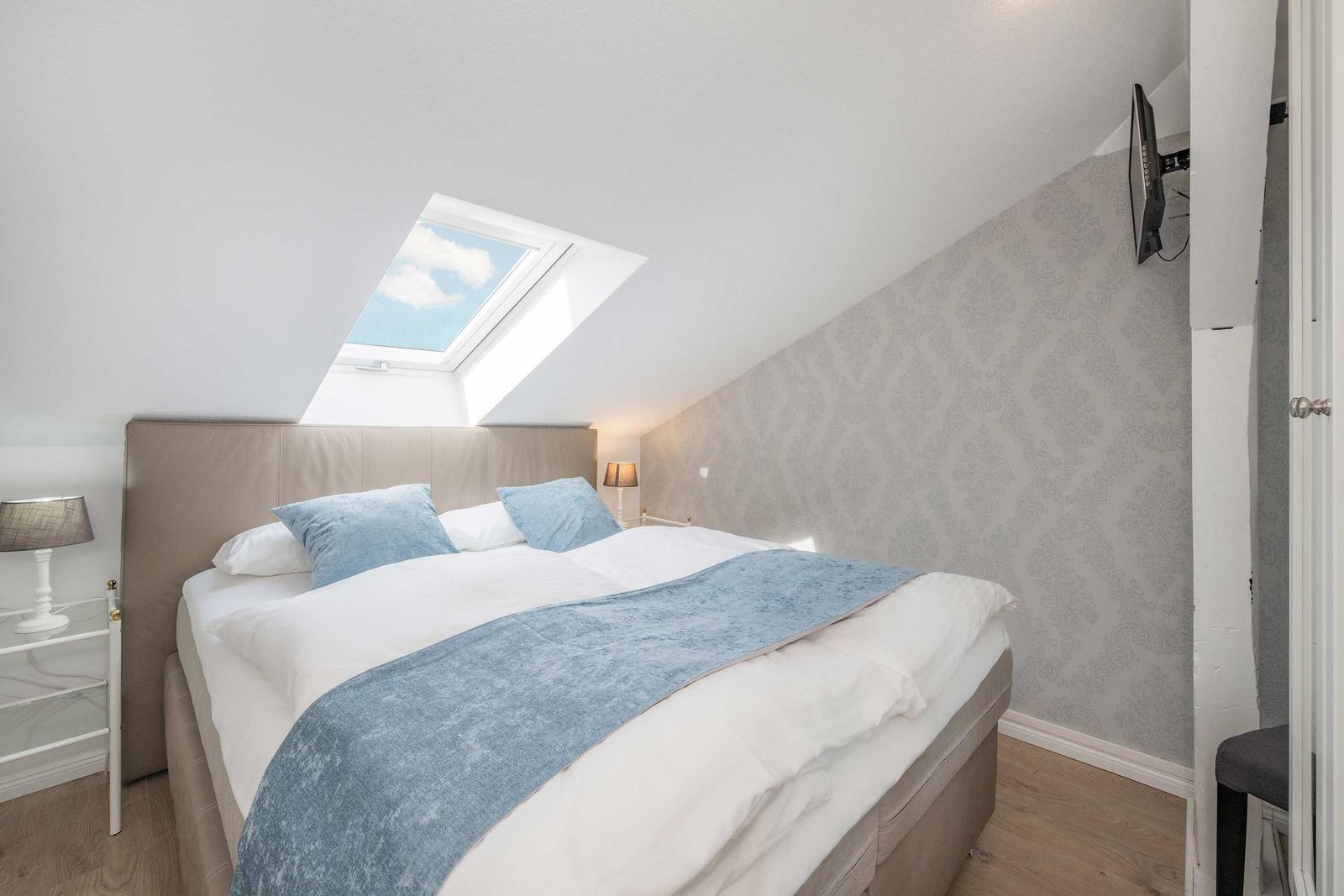 Schlafzimmer mit Dachschrägen, Dachfenster und Bett mit blauer Decke.