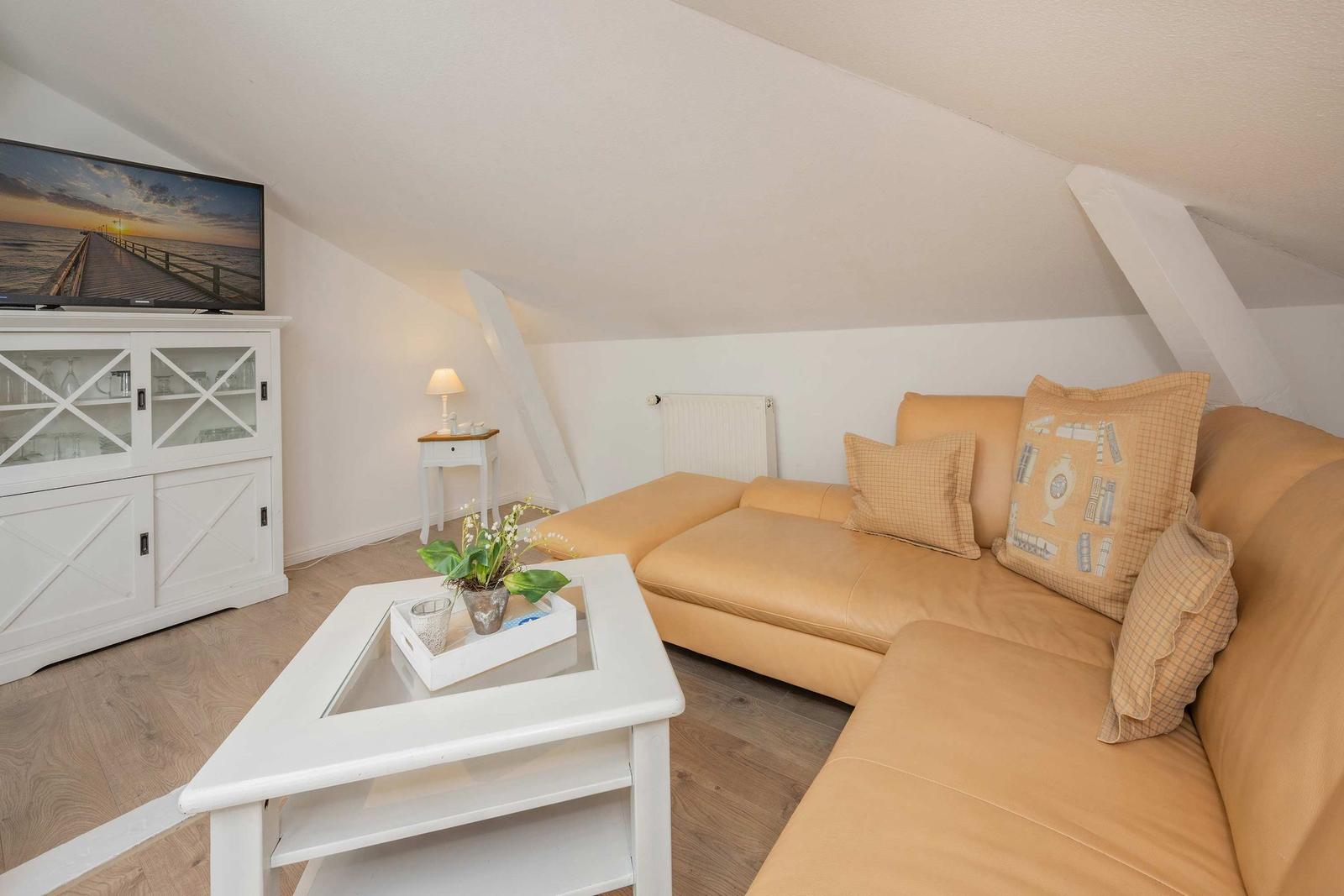 Ein Wohnzimmer mit einem hellbraunen Sofa, einem weißen Couchtisch und einer TV-Einrichtung.