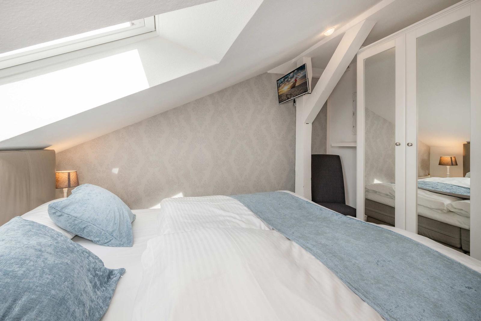 Schlafzimmer mit Dachfenster, Bett, Kleiderschrank und Wand-TV.