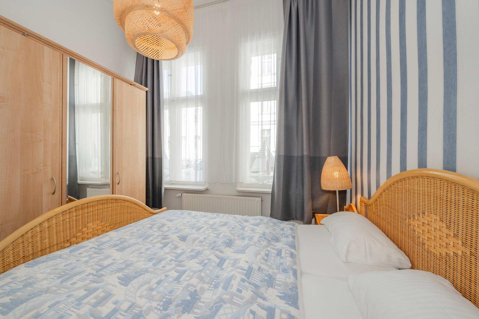 Schlafzimmer mit Bett, Kleiderschrank und Fenster mit Vorhängen.