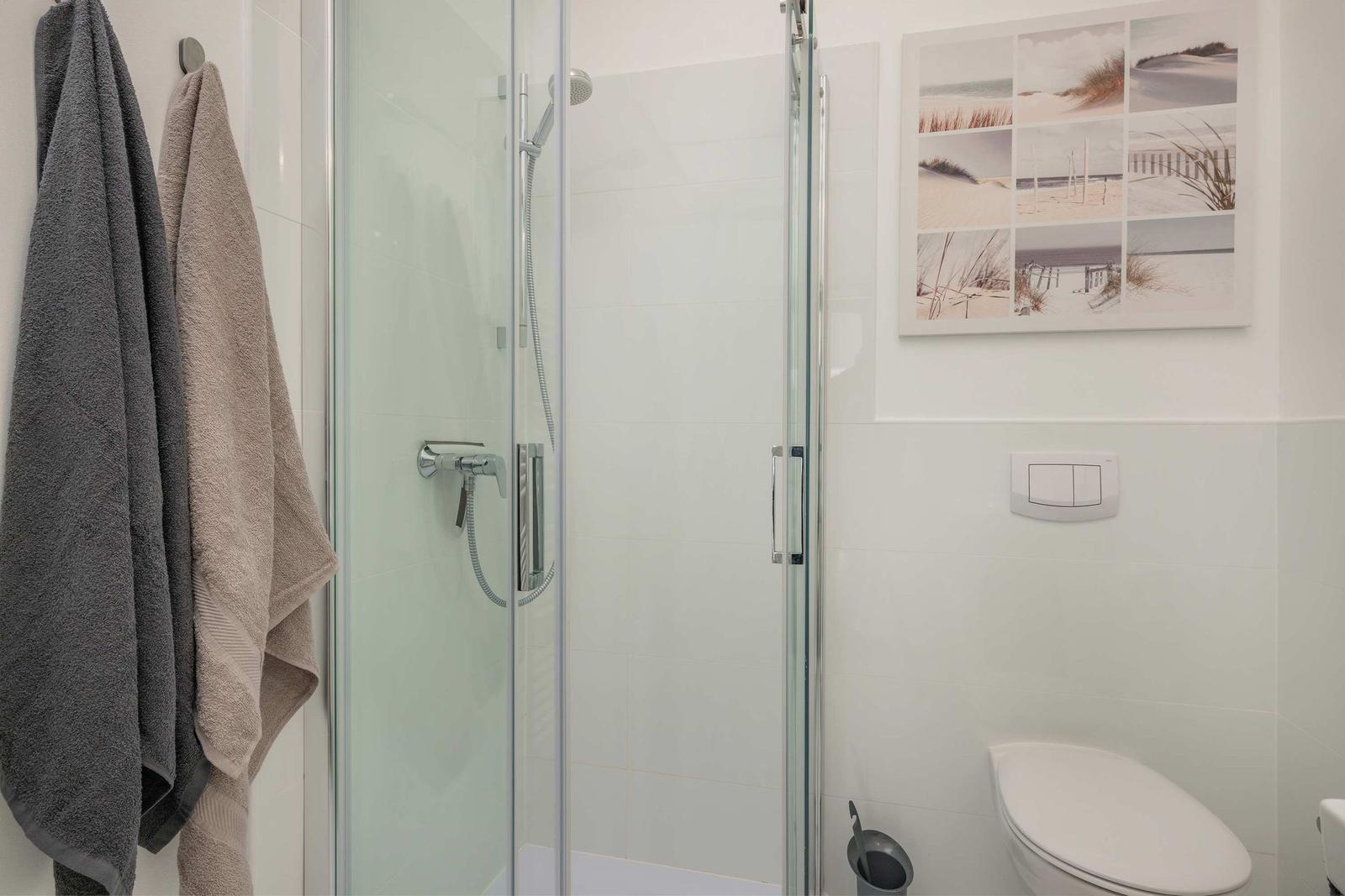 Dusche mit Glaswand, Toilette und Wandbild mit Strandmotiven.