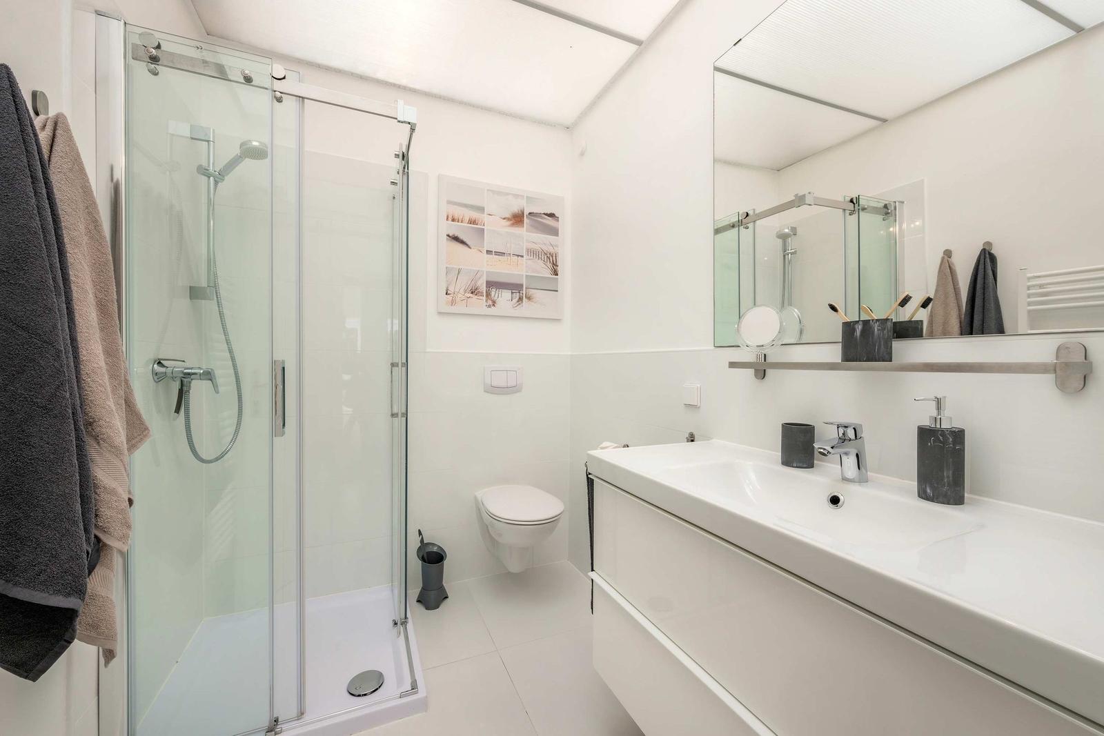 Badezimmer mit Dusche, Waschbecken und Toilette. Moderne Einrichtung und hell.