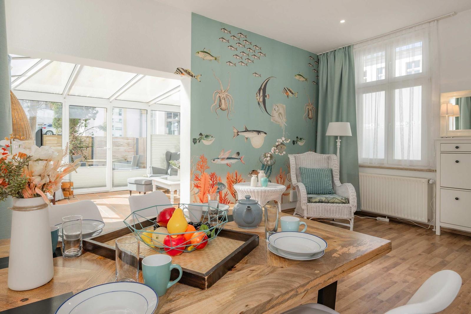 Esszimmer mit Holztisch, Wand mit Fischmotiven und Sicht auf Terrasse.
