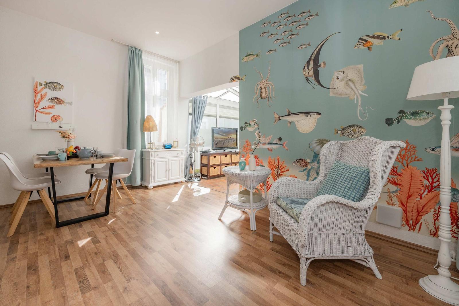 Wohnzimmer mit Fischmotiv-Wand, weißen Wicker-Sofa und Holzboden.