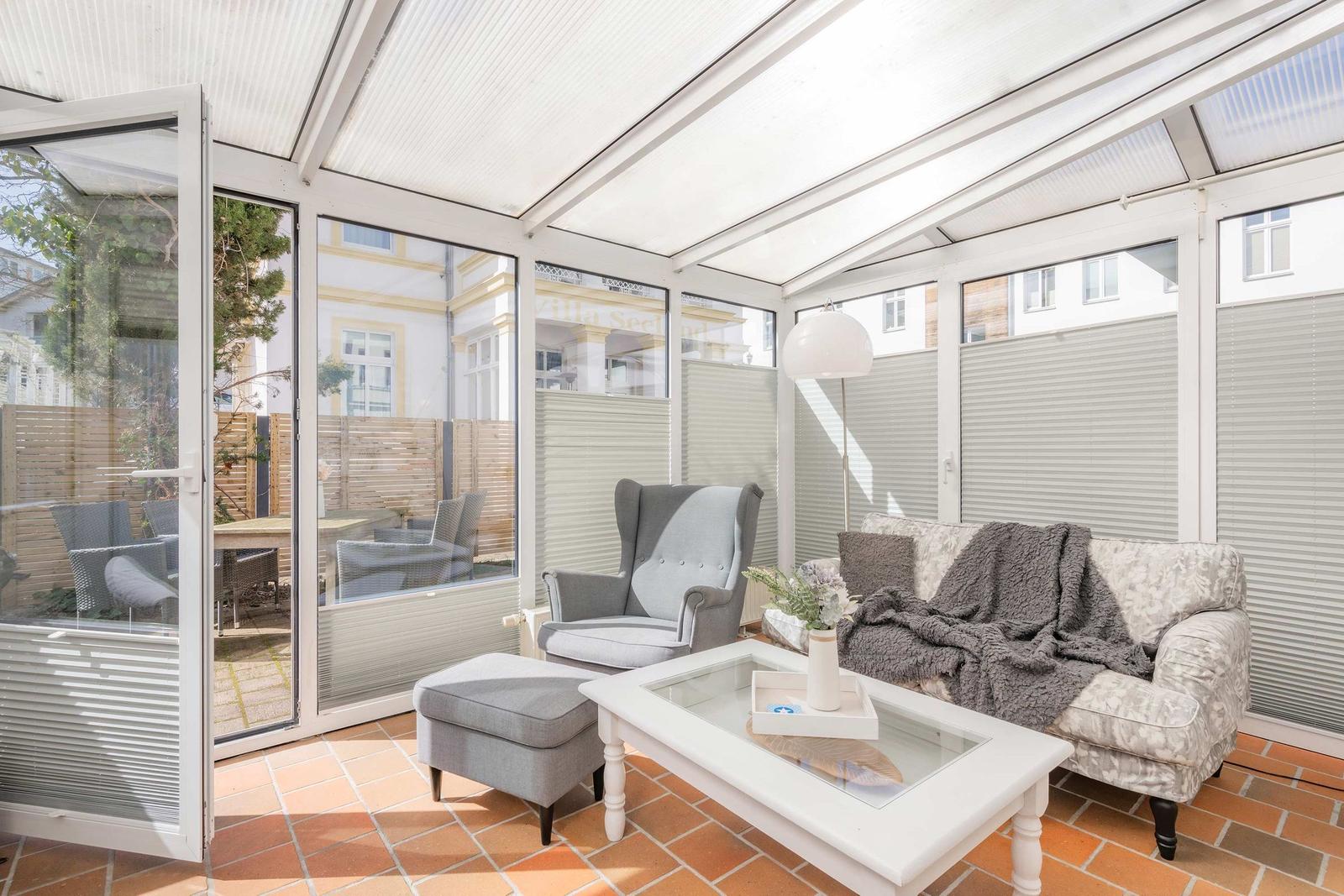 Terrassenbereich mit Sitzmöbeln, Glas-Tisch und Terrakottboden. Durchgehendes Glasdach und Fensterfront.