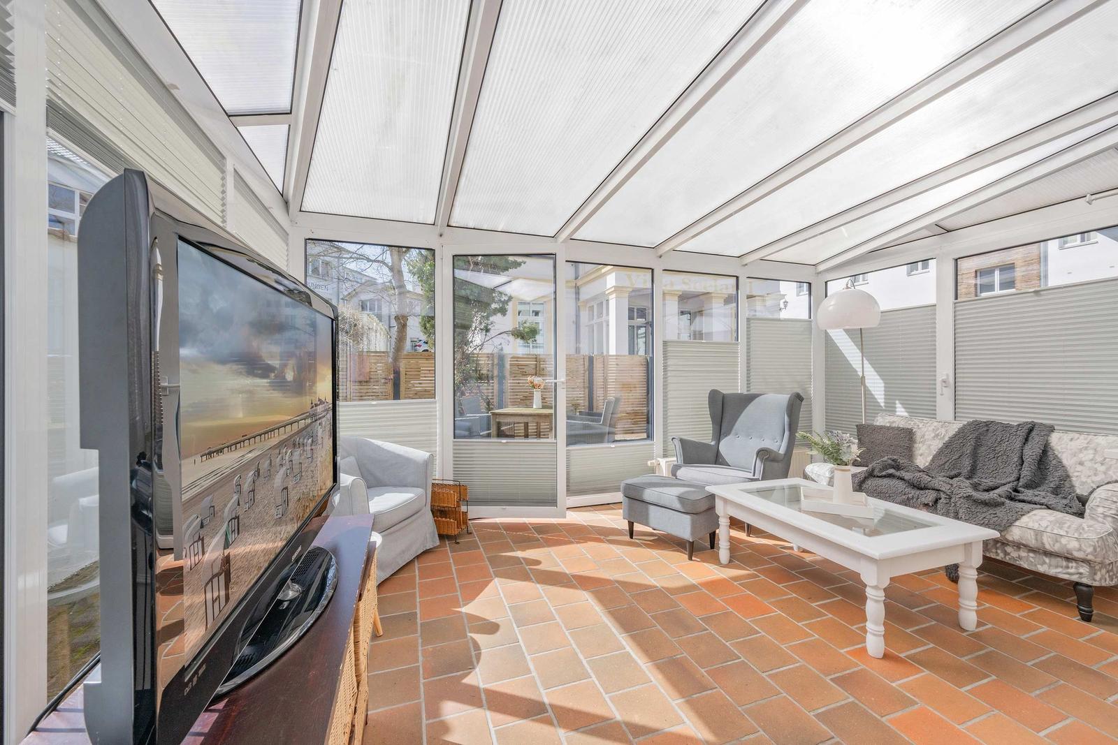 Terrassenbereich mit Fernseher, Sofa und Sitzgelegenheiten auf Terrakottaboden.