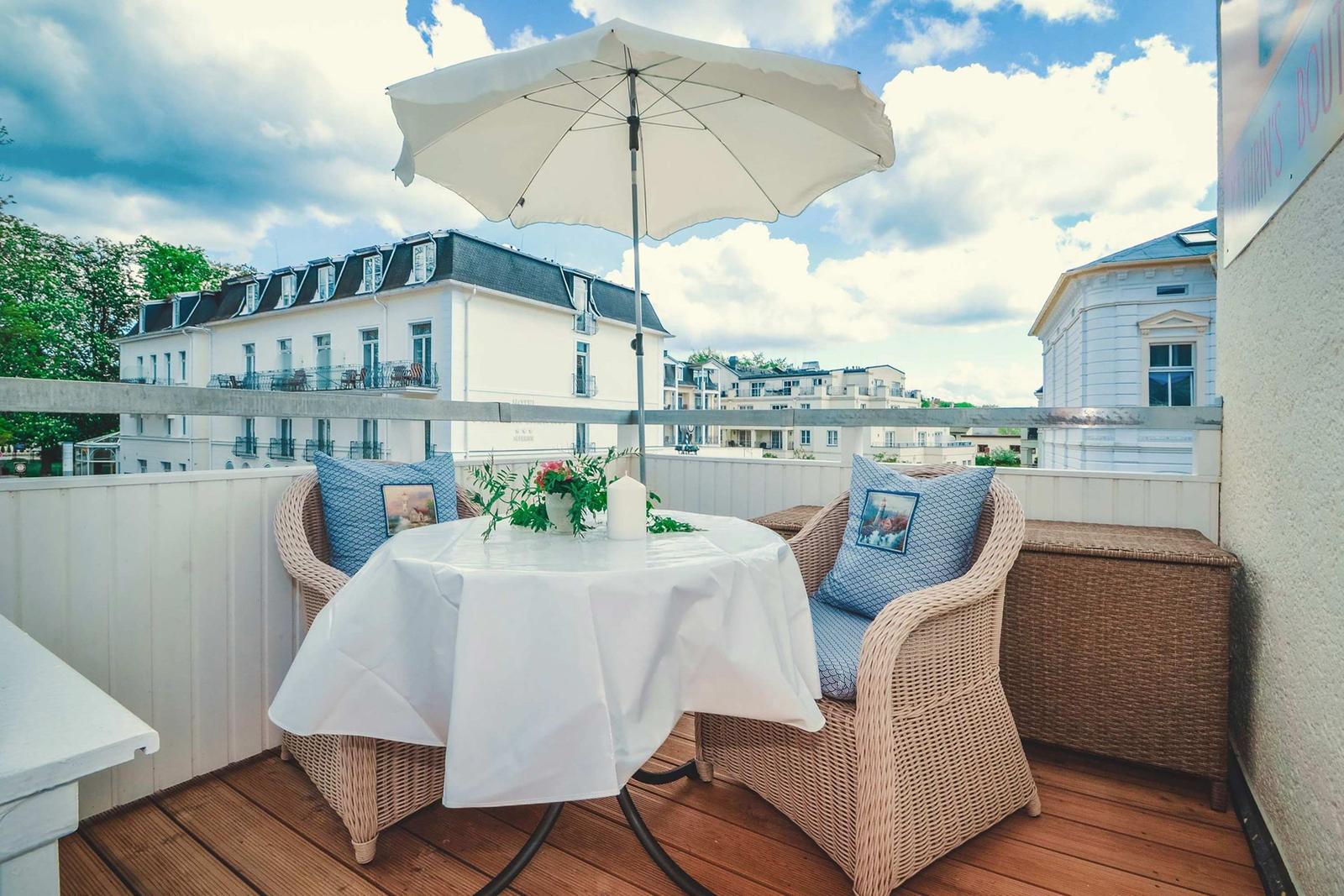 Terrace with table, chairs, and umbrella. View of houses and trees.