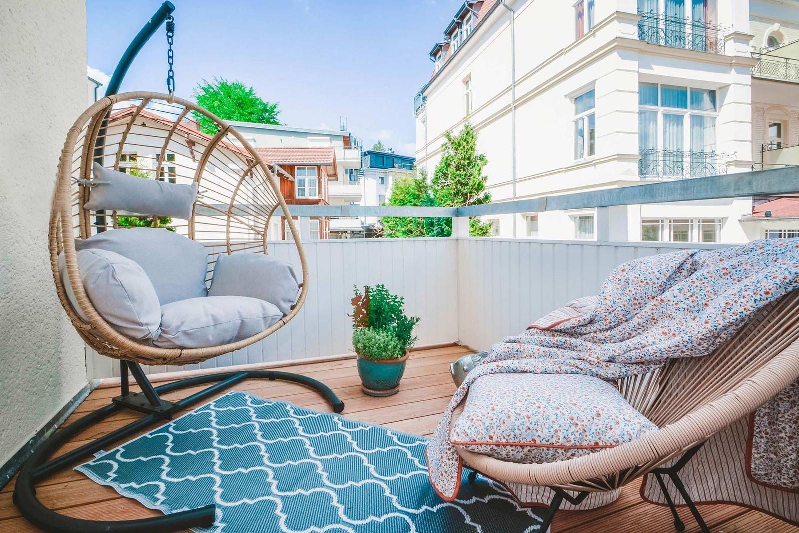 Terrace with hanging chair and lounge chair, blue rug, and plant.