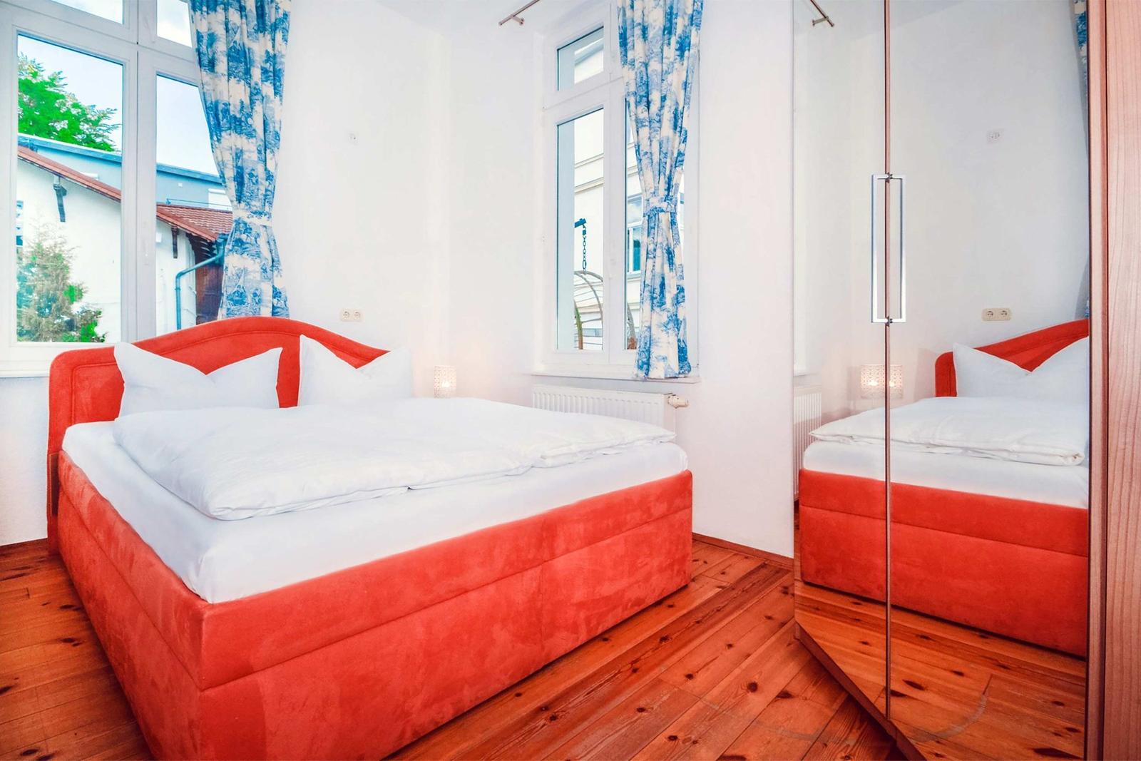 Bedroom with red bed, wooden floor, and blue curtains on windows.