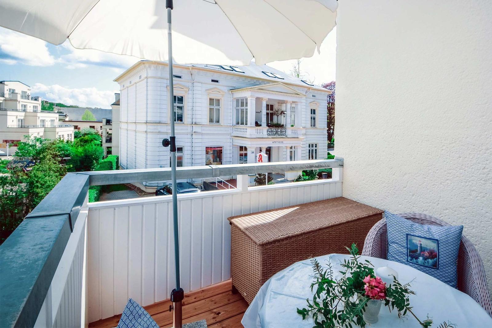 Terrace with table, chairs, and umbrella. View of a white house with balcony.