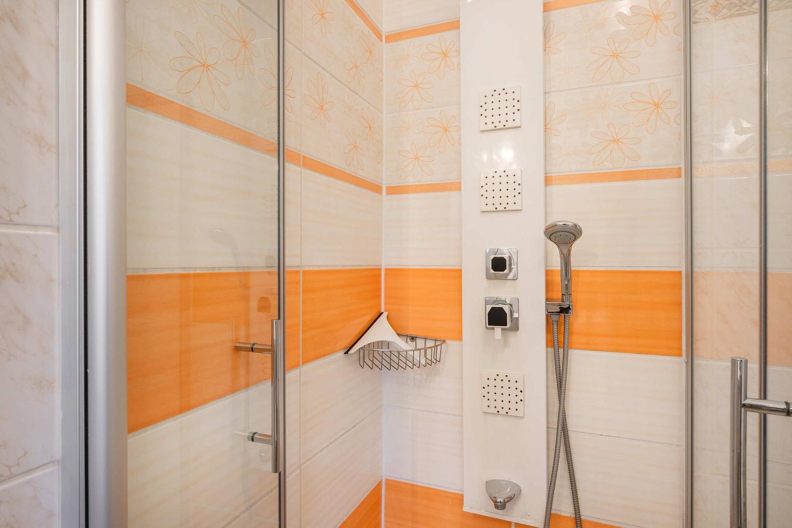 Dusche mit Glaswand, orangefarbenen Fliesen und Duschbrause
