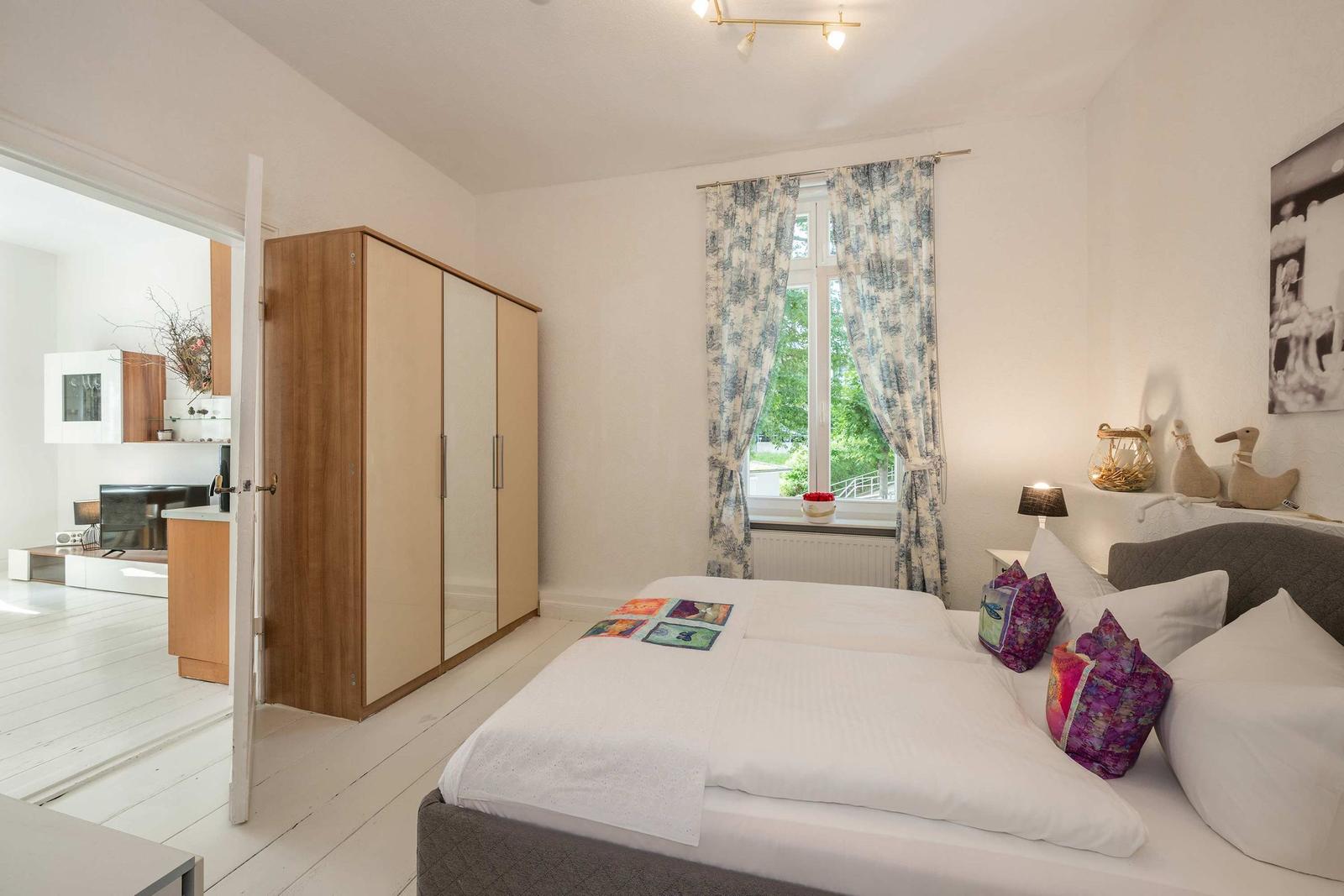 Schlafzimmer mit Bett, Kleiderschrank und Fenster mit Blick nach draußen.