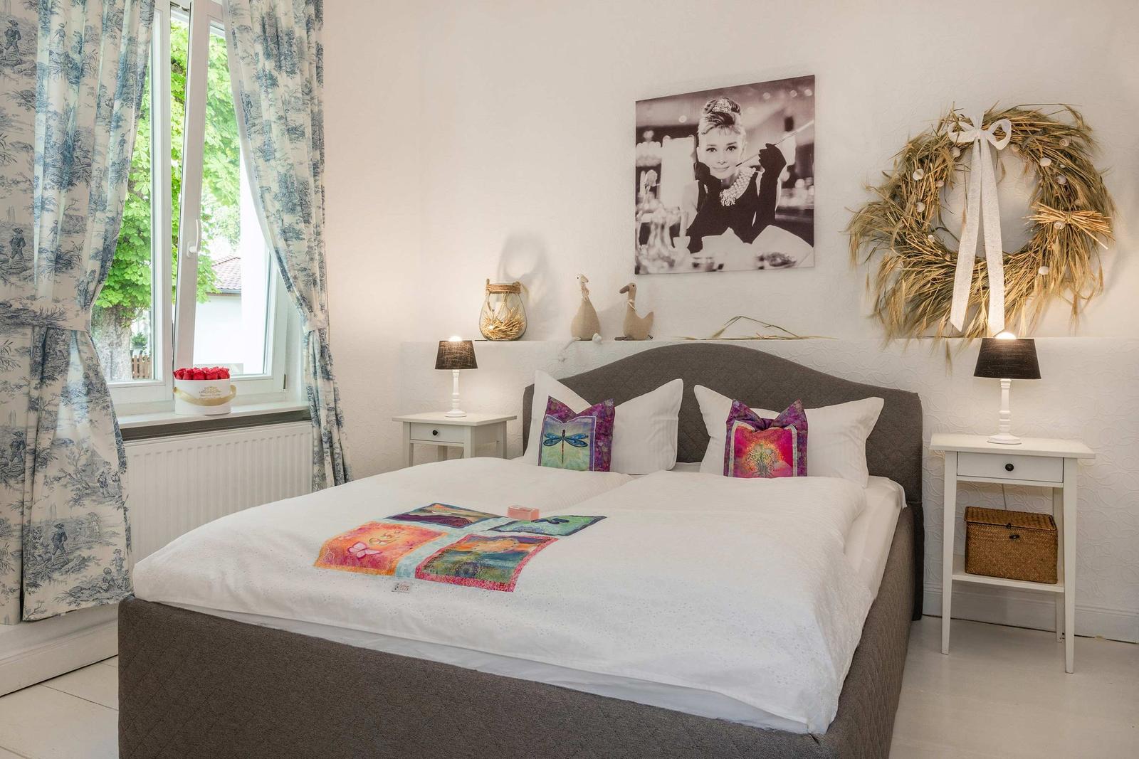 Schlafzimmer mit Bett, Nachttischen und Fenster mit Vorhängen.