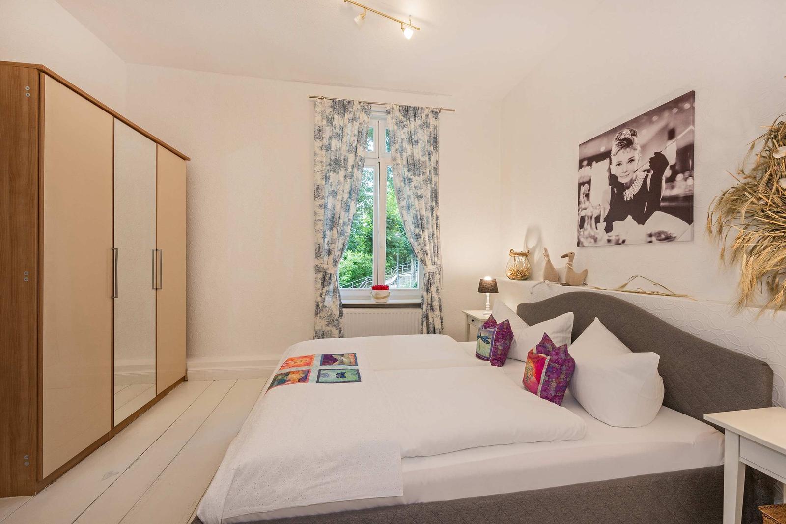 Schlafzimmer mit Bett, Kleiderschrank und Fenster mit Blick auf Grün.