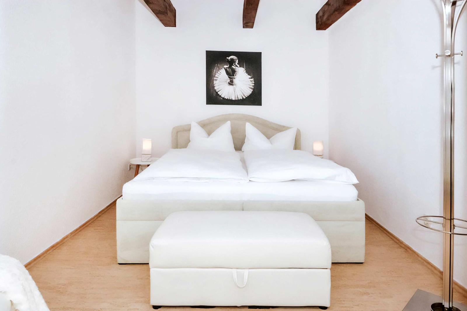 Bedroom with white bed, wooden beams, and wall picture of a ballerina.