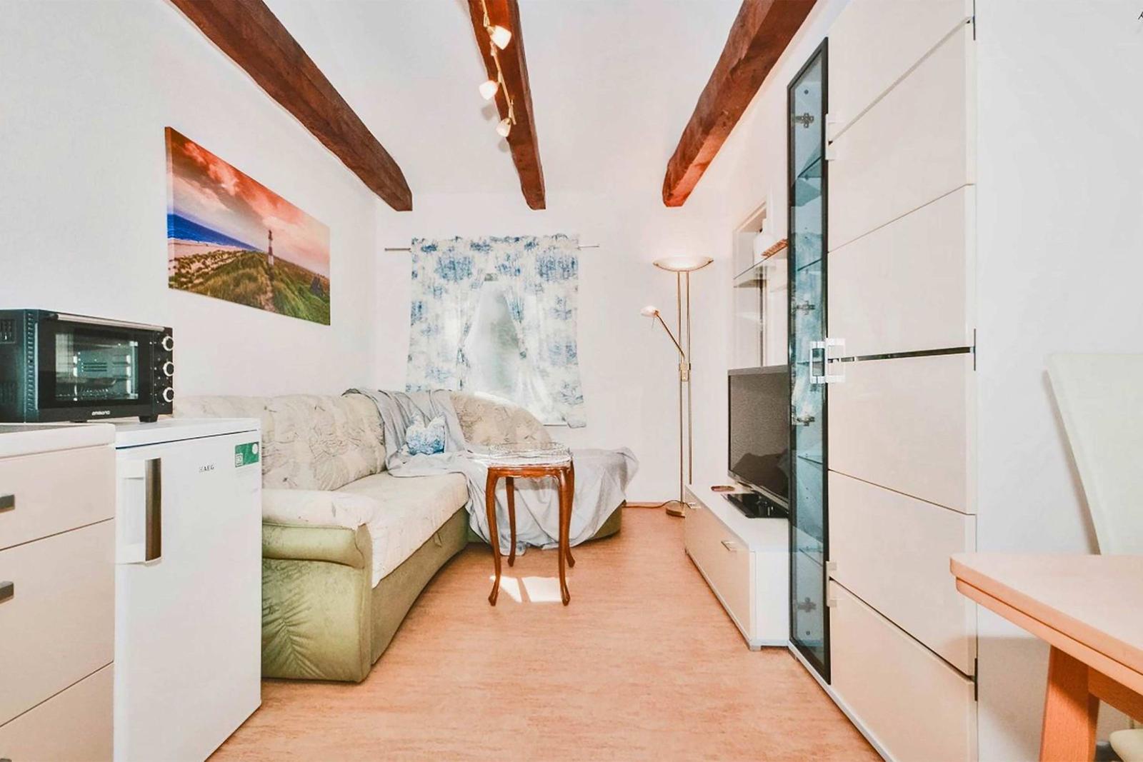 Living room with sofa, kitchenette, and TV. Wooden beams on the ceiling.