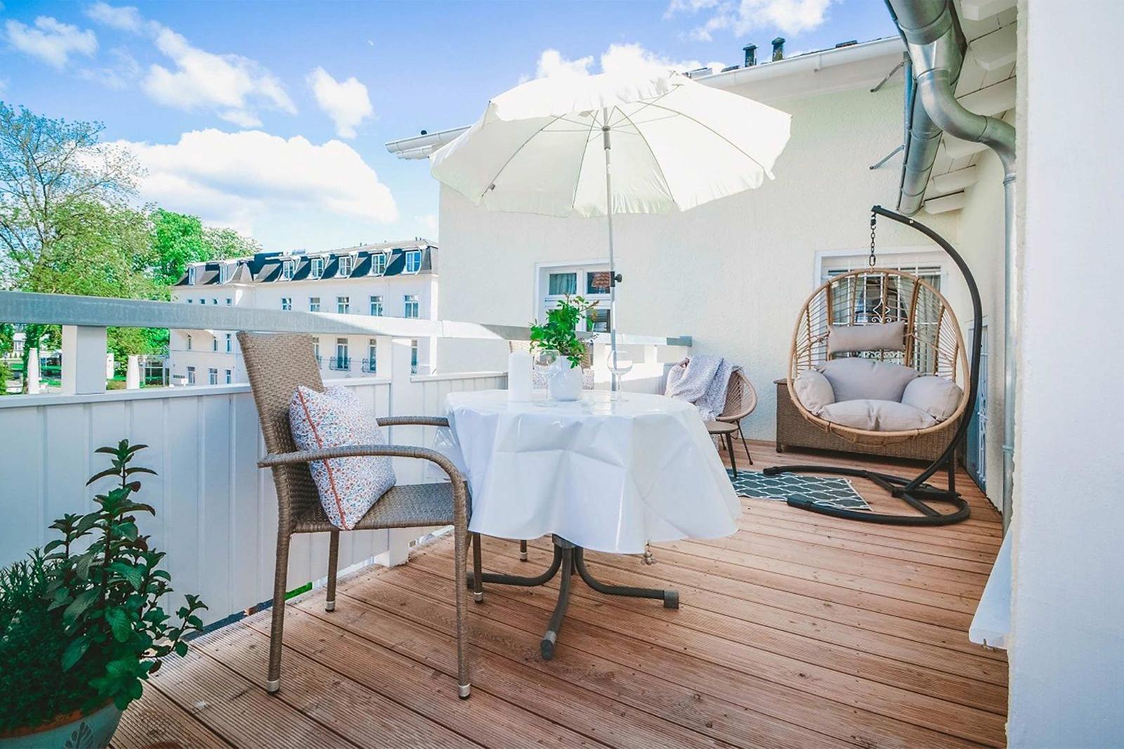 Terrace with table, chairs, umbrella, and hanging chair. Wooden deck and white railing.
