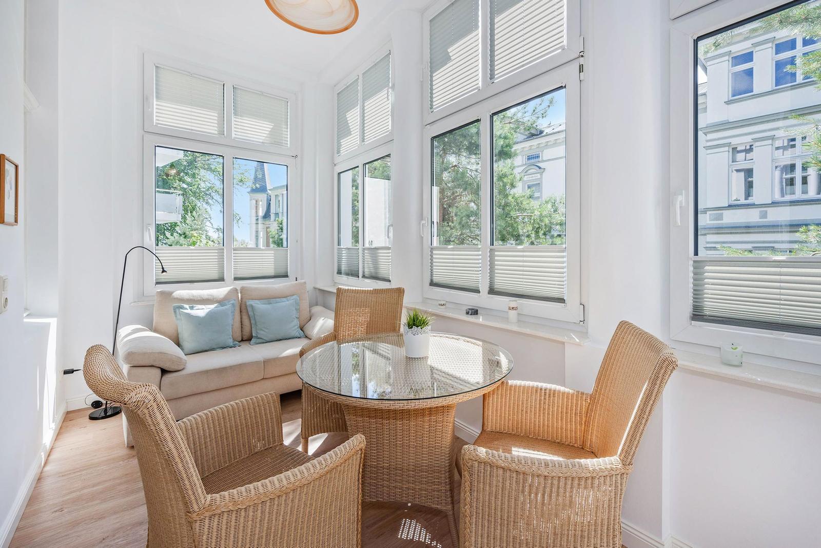 A room with sofa, round table, and chairs. Large windows with view of buildings.