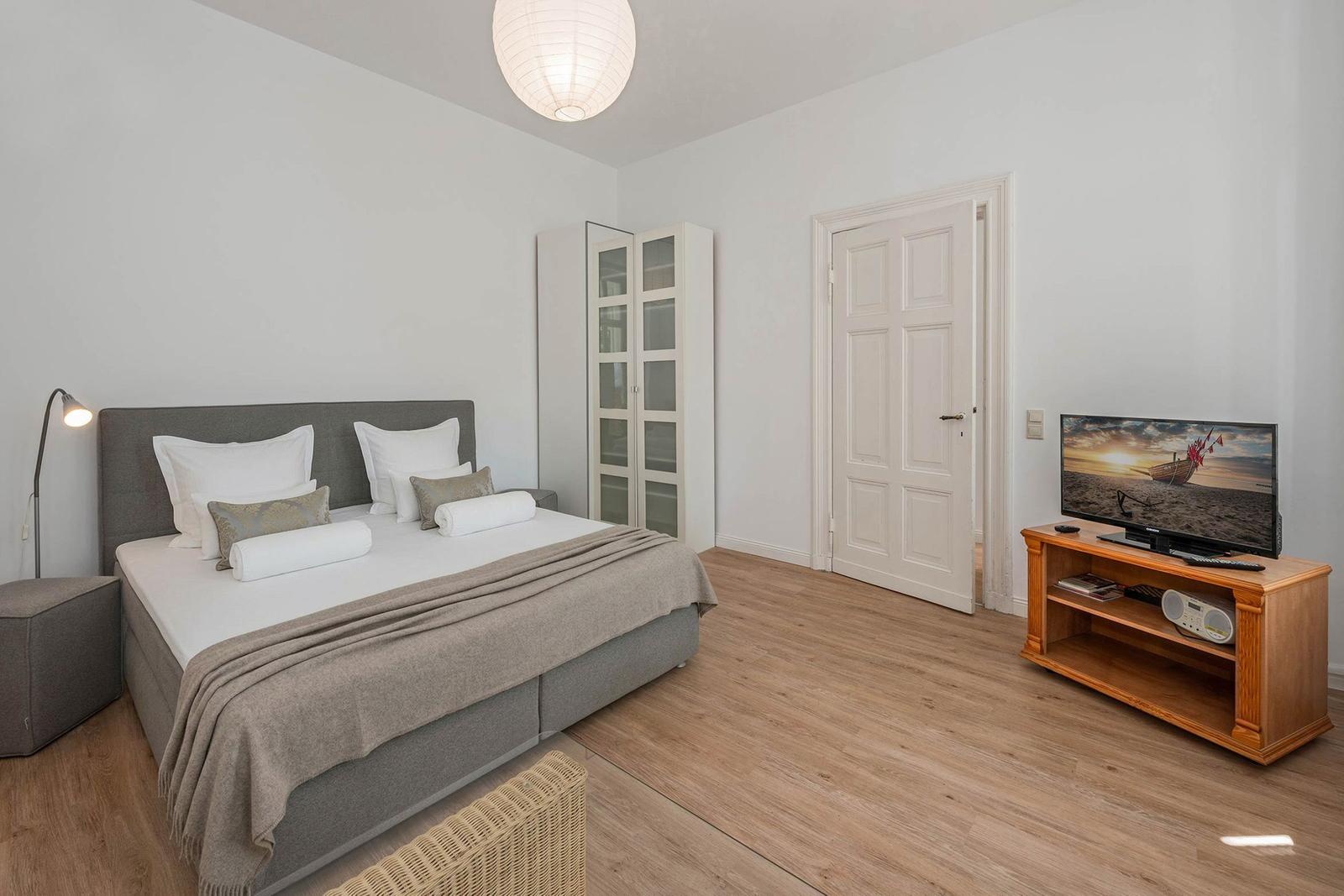Bedroom with bed, TV, and closet. Wooden floor and white walls.