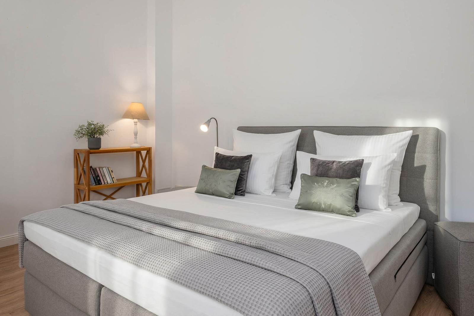 A bed with pillows, sheets, and a blanket. Next to the bed is a nightstand with a lamp.