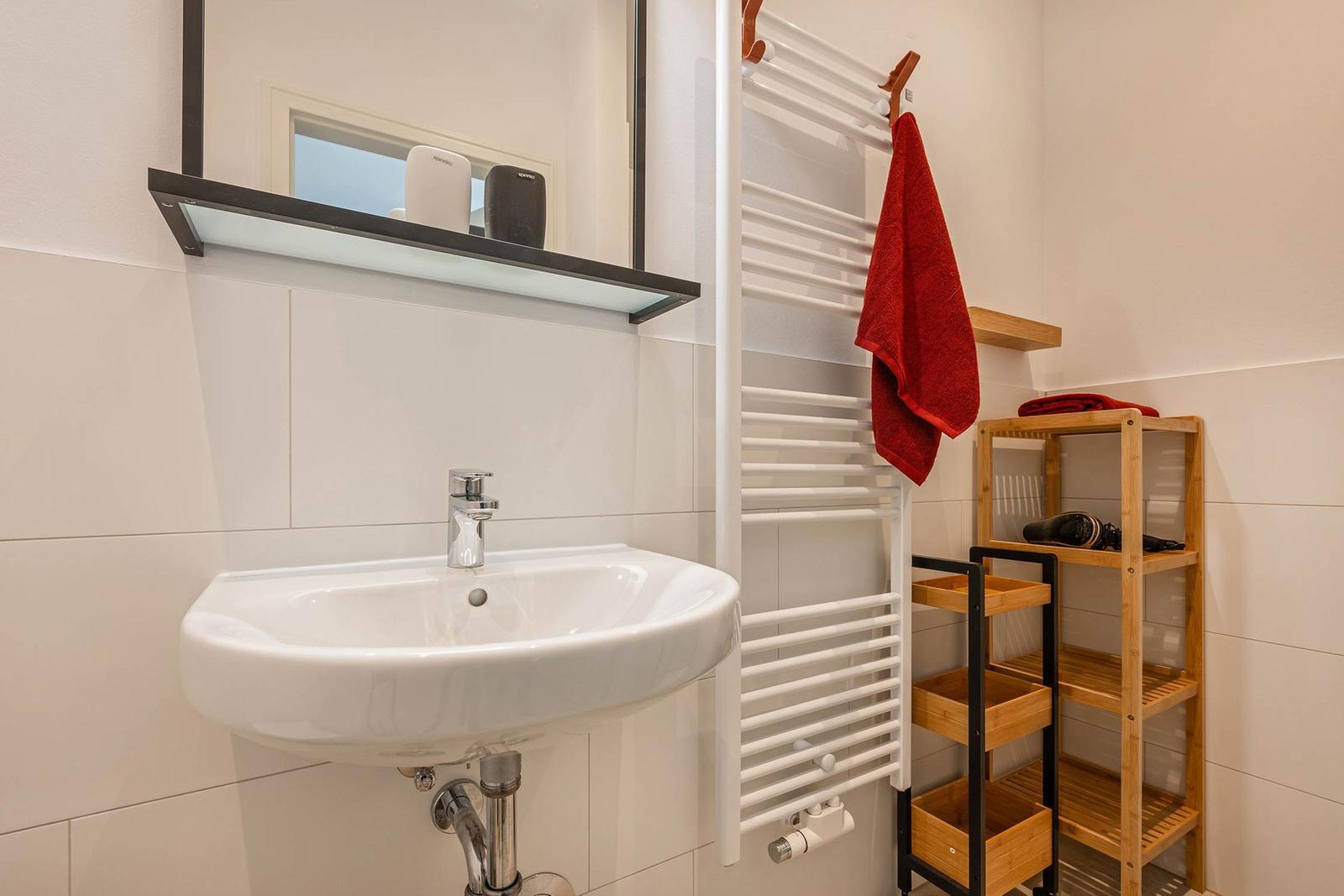 Bathroom with sink, mirror, towel rack, and wooden shelf.