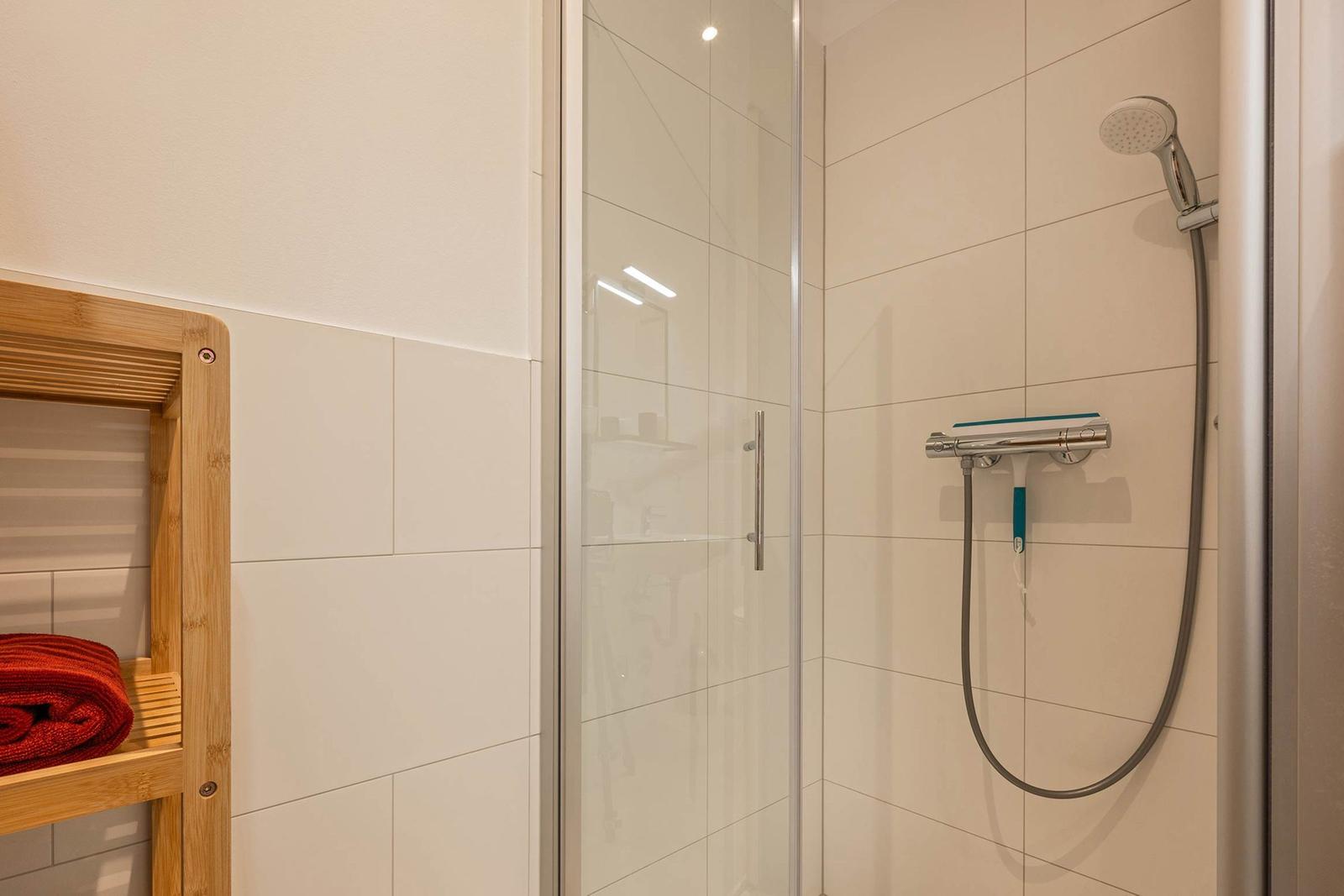 Shower with glass enclosure, shower head, and wooden shelf with towel.