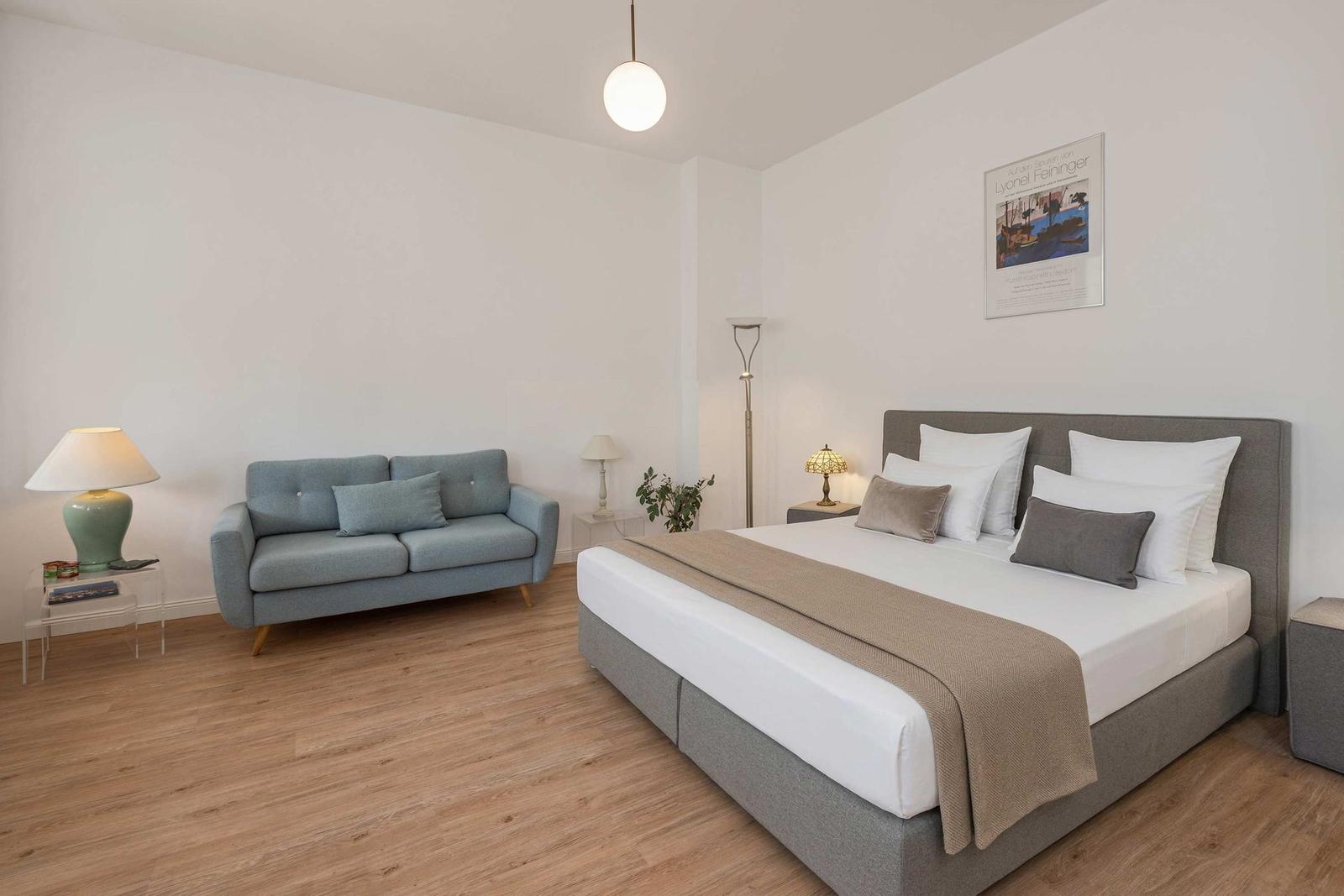 Bedroom with bed, sofa, and lamp. Wooden floor and wall poster.