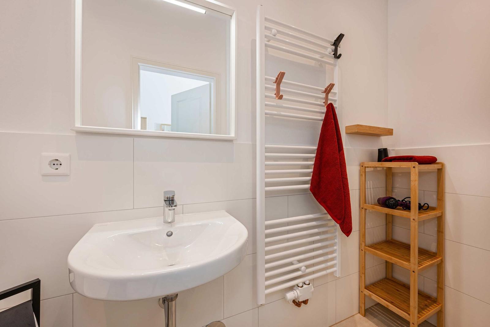 Bathroom with sink, mirror, heater, and wooden shelf.