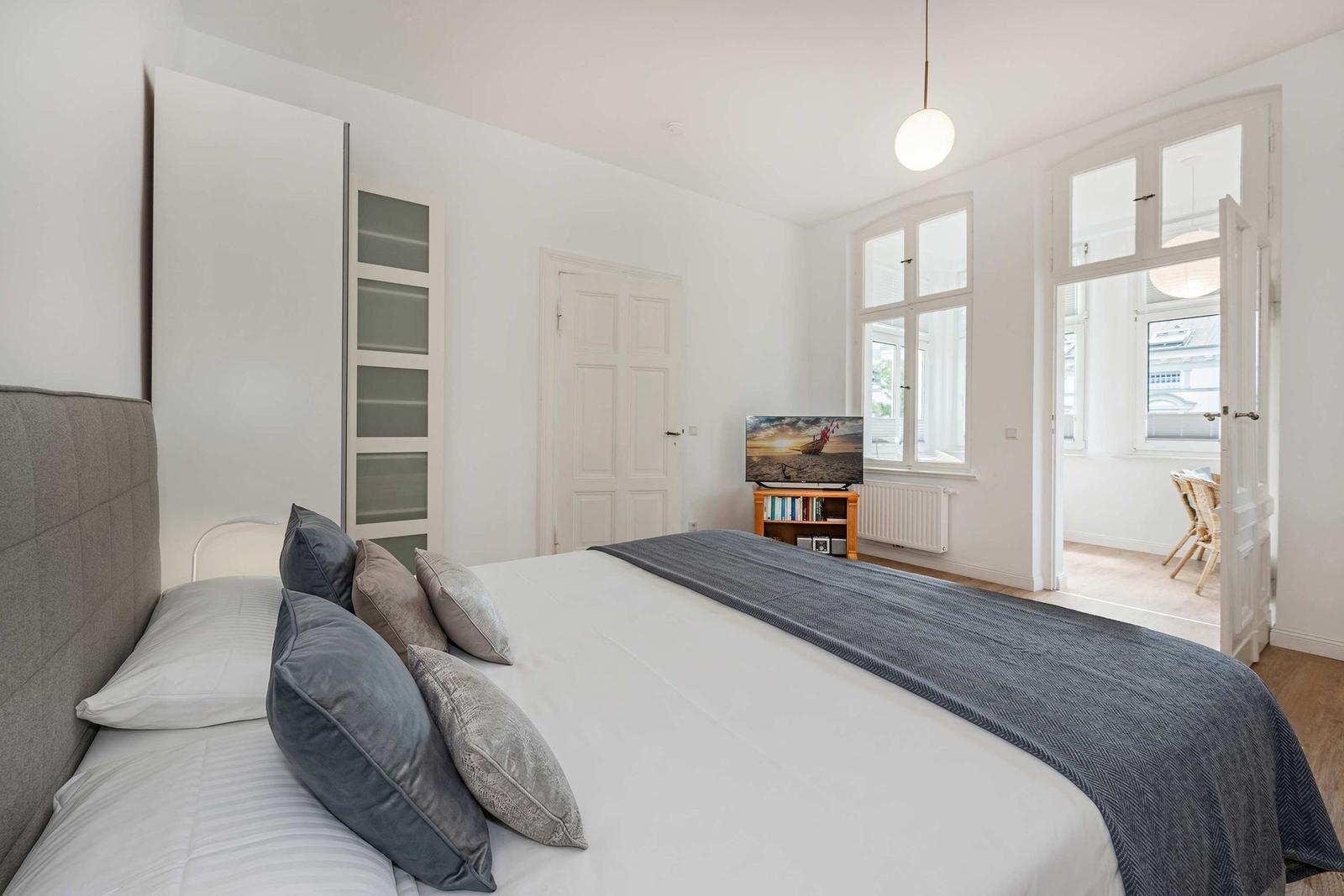Bedroom with large bed, TV, and windows. Door leads to living area.