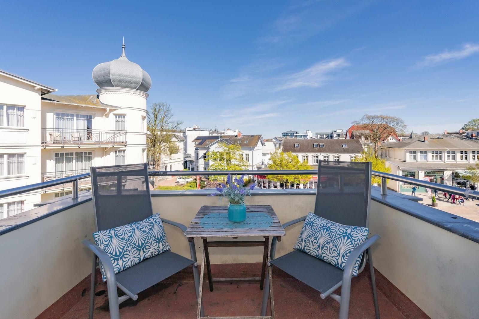 Terrasse mit zwei Stühlen und Tisch. Blick auf Gebäude und blauen Himmel.